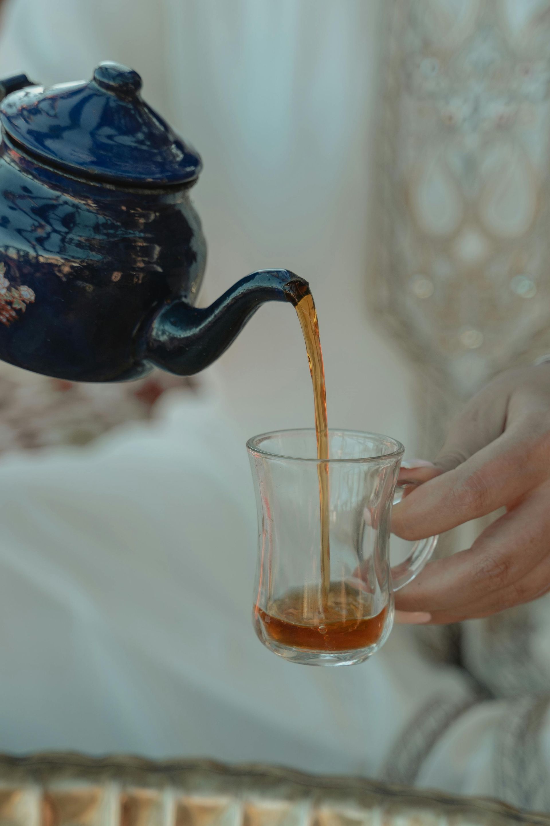 A person is pouring tea from a teapot into a glass.