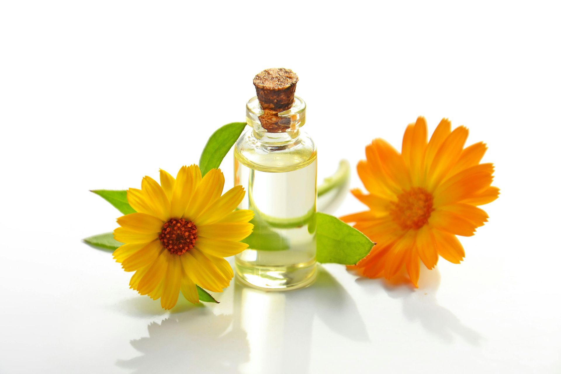 A bottle of essential oil next to two yellow flowers