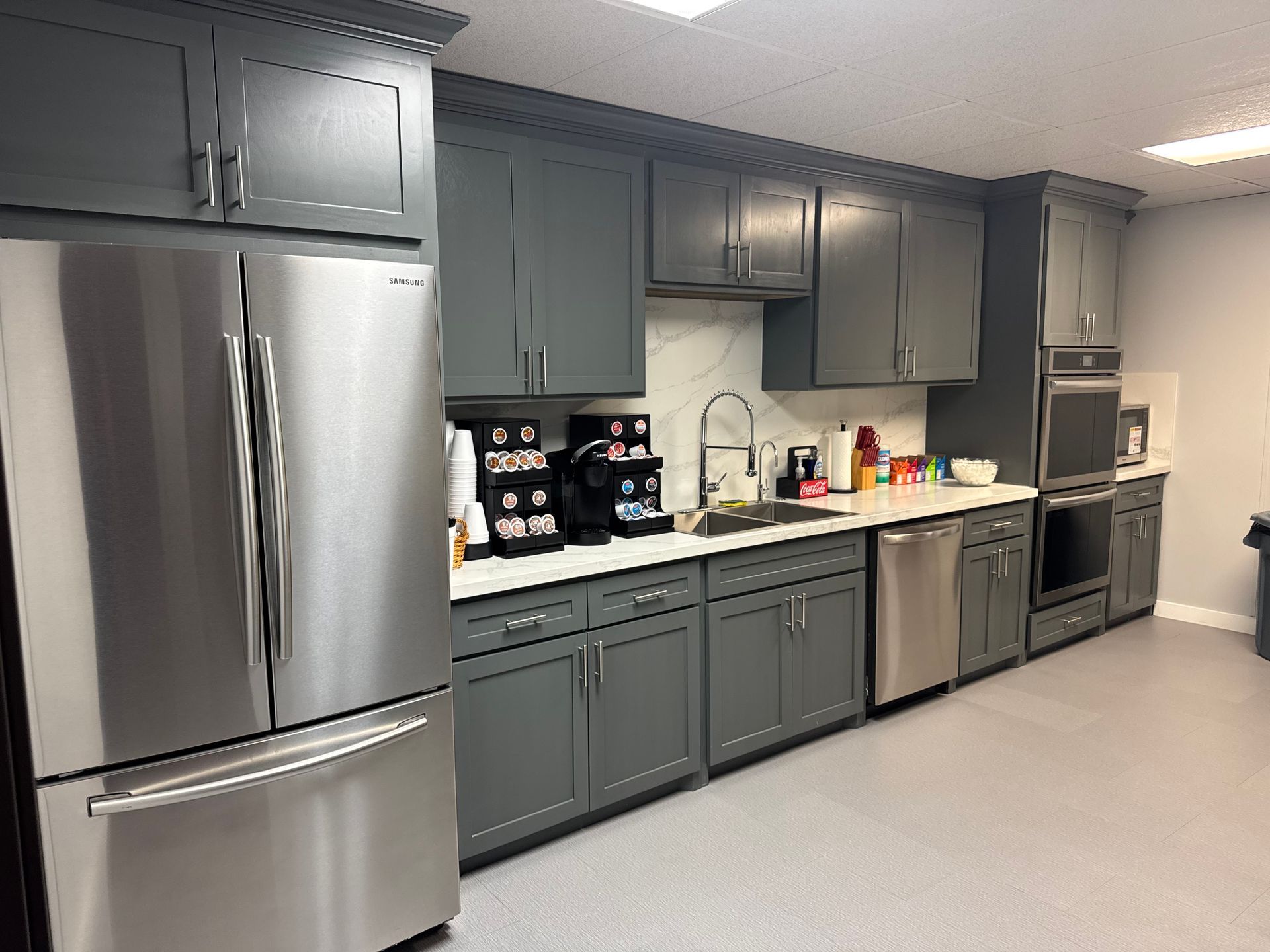 A modern office kitchen with gray cabinets, stainless steel appliances, and a coffee station.