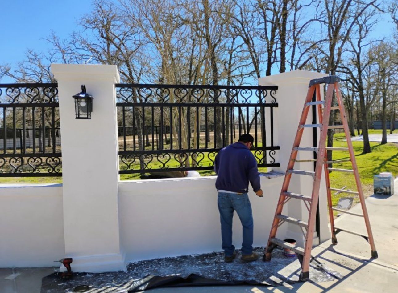A man is standing next to a ladder painting a fence.