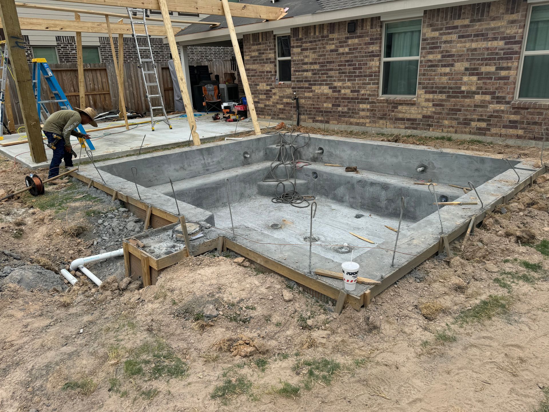 A man is working on a swimming pool in the backyard of a house.