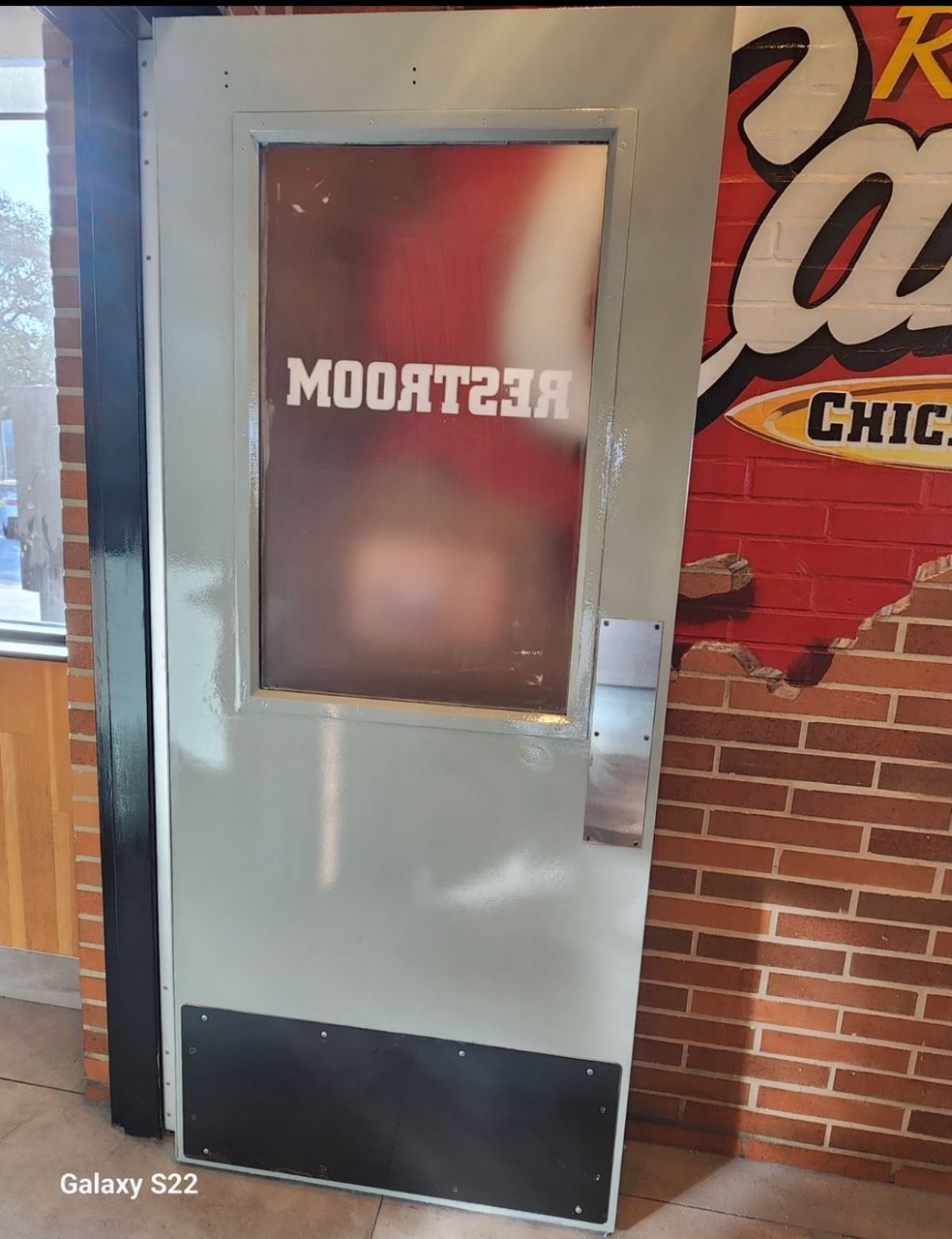 A galaxy s22 is sitting next to a door with a brick wall behind it.