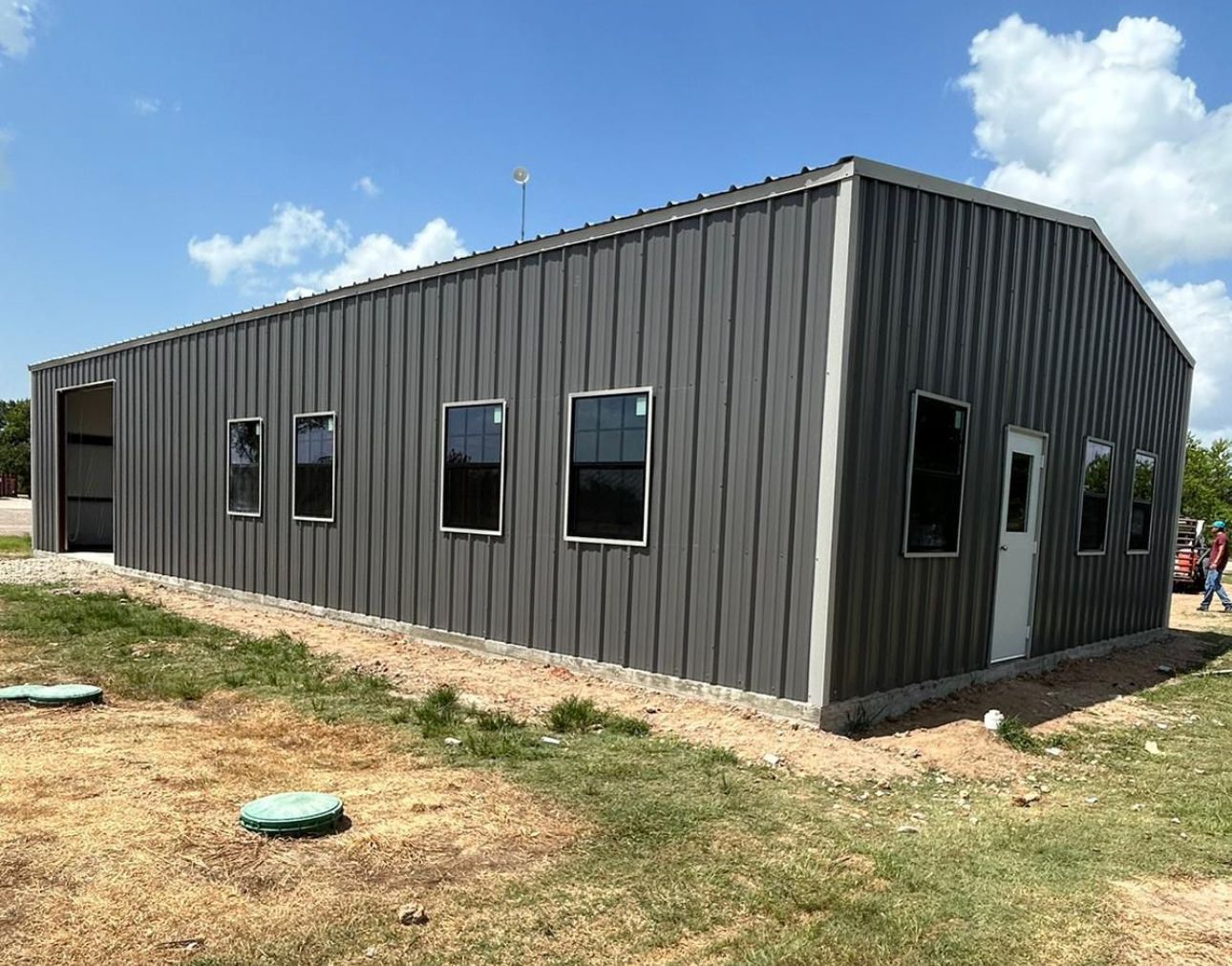A large metal building with a lot of windows is sitting in the middle of a grassy field.