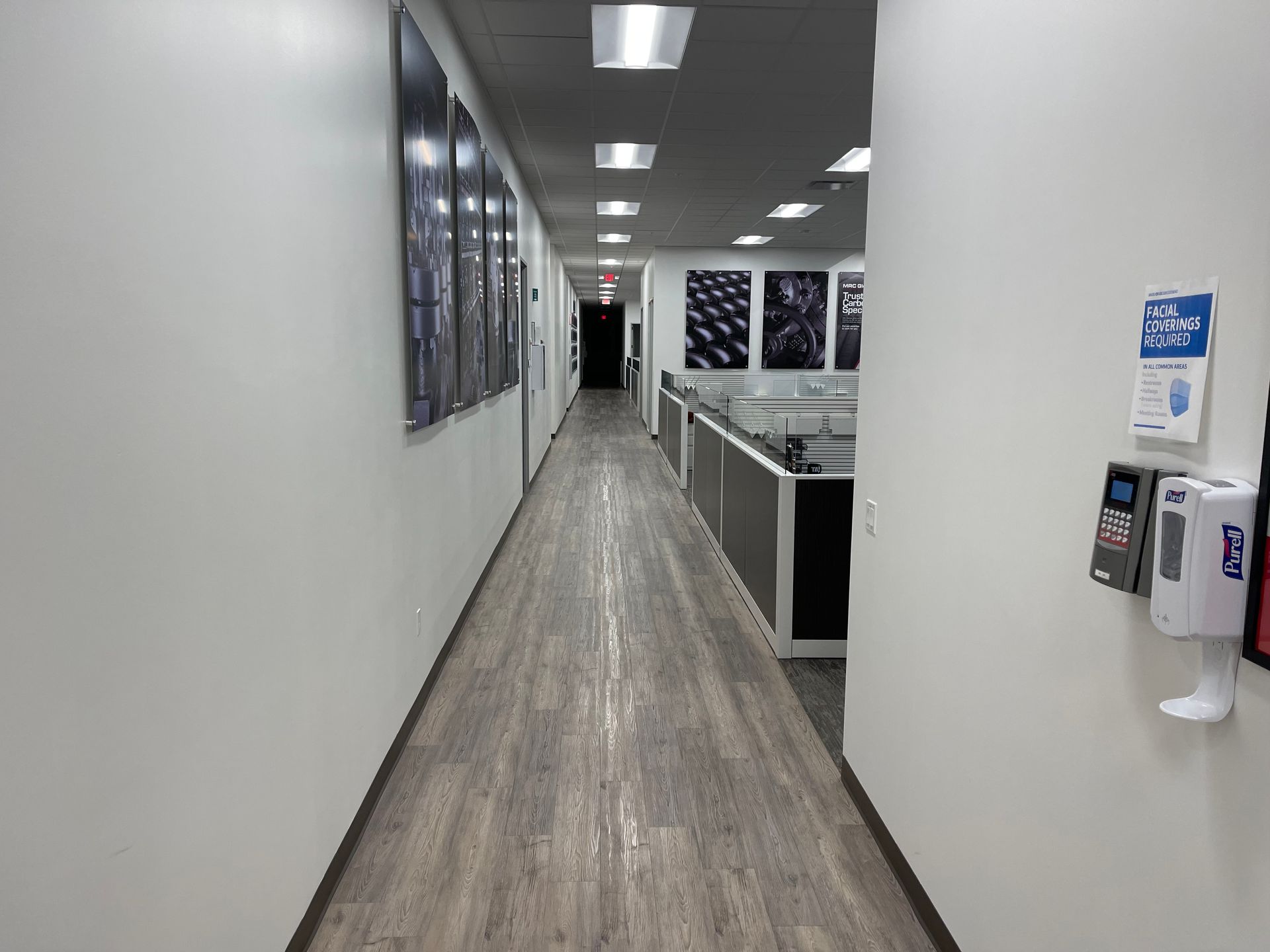 A long hallway in an office building with a hand sanitizer dispenser on the wall.