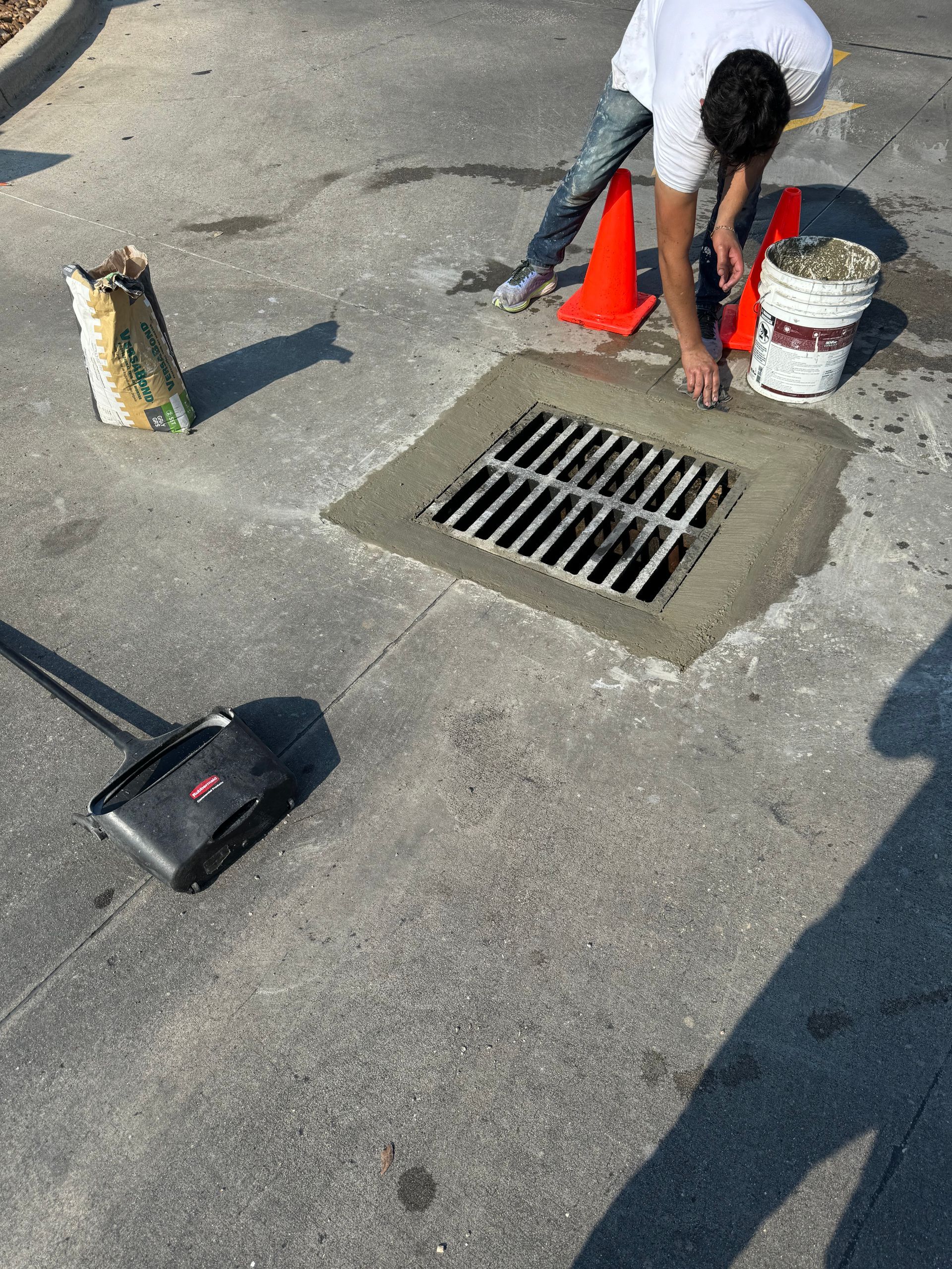 A man is working on a drain on the side of the road.