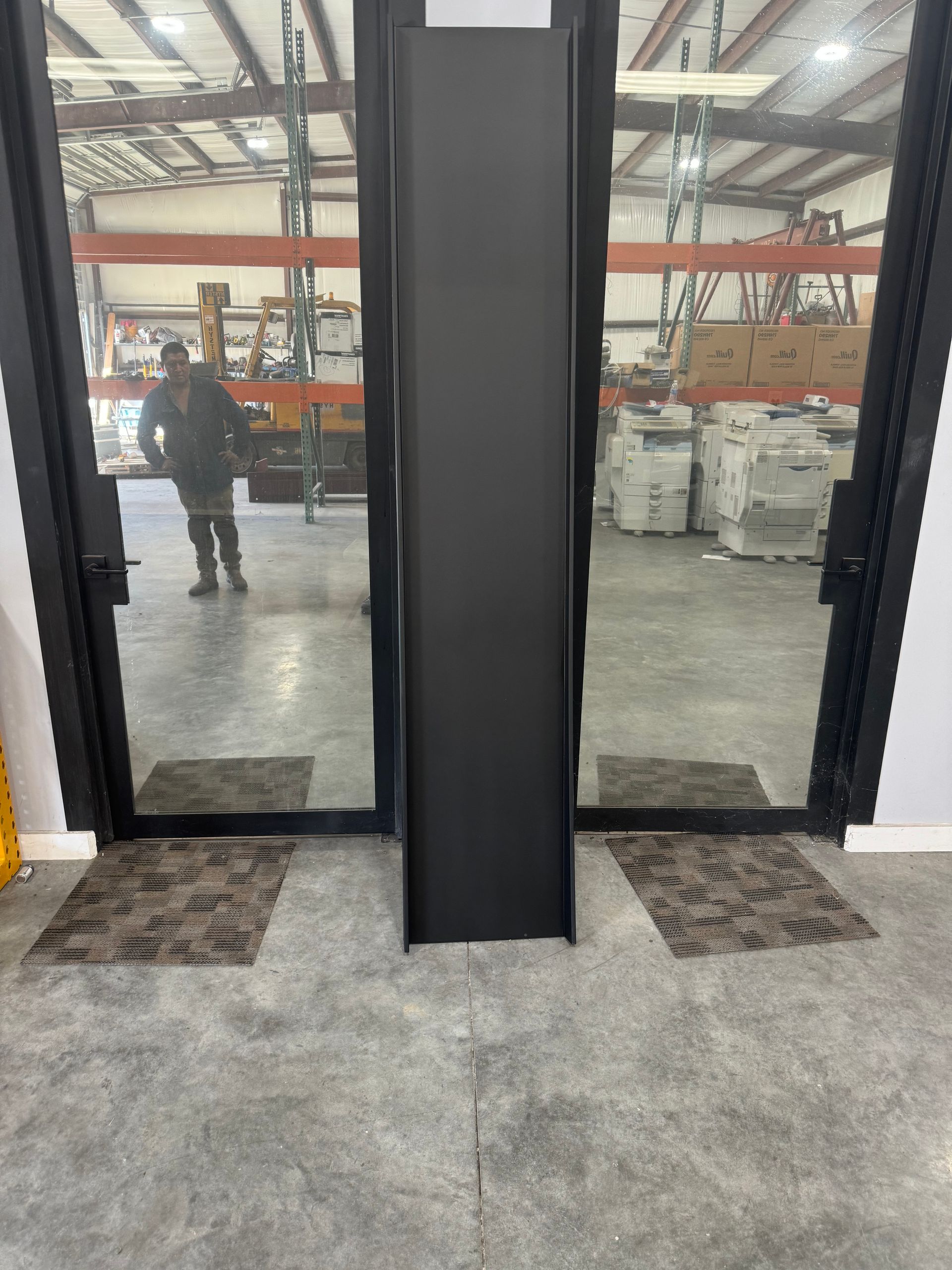 A man is standing in front of a glass door in a warehouse.