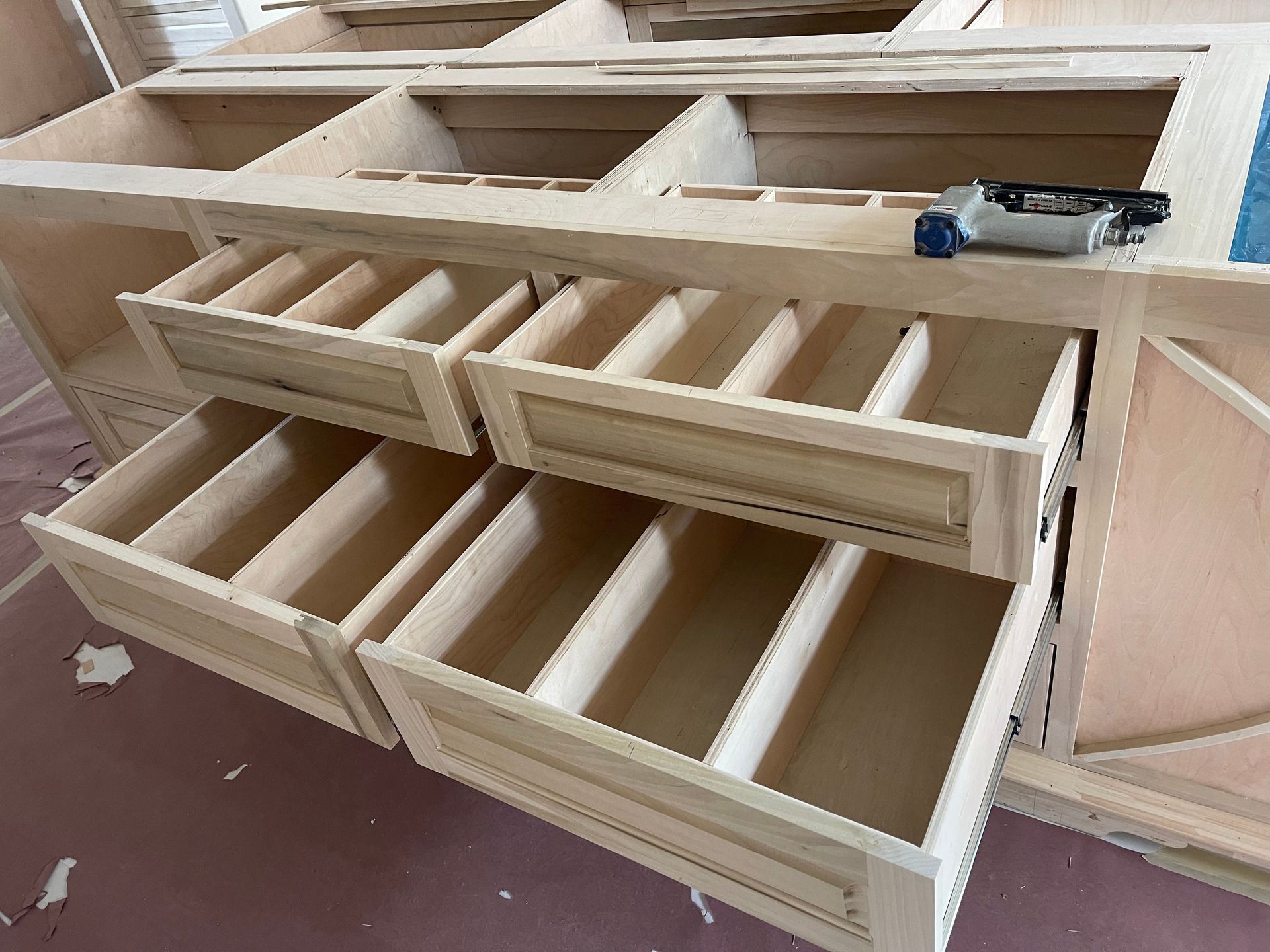 Wooden cabinet under construction with open drawers, showing internal dividers and a nail gun.