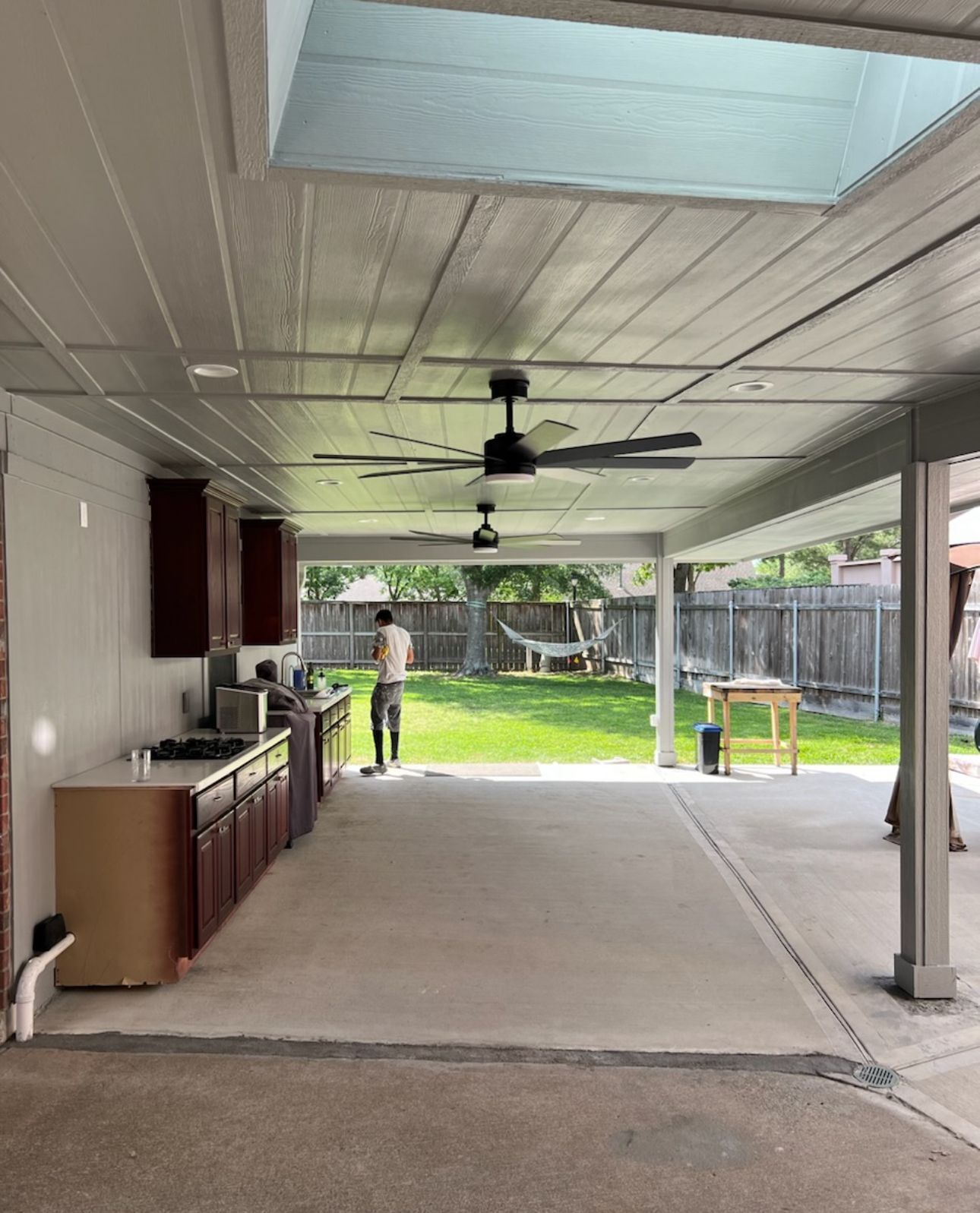 A man is standing in a kitchen under a covered patio with a ceiling fan.