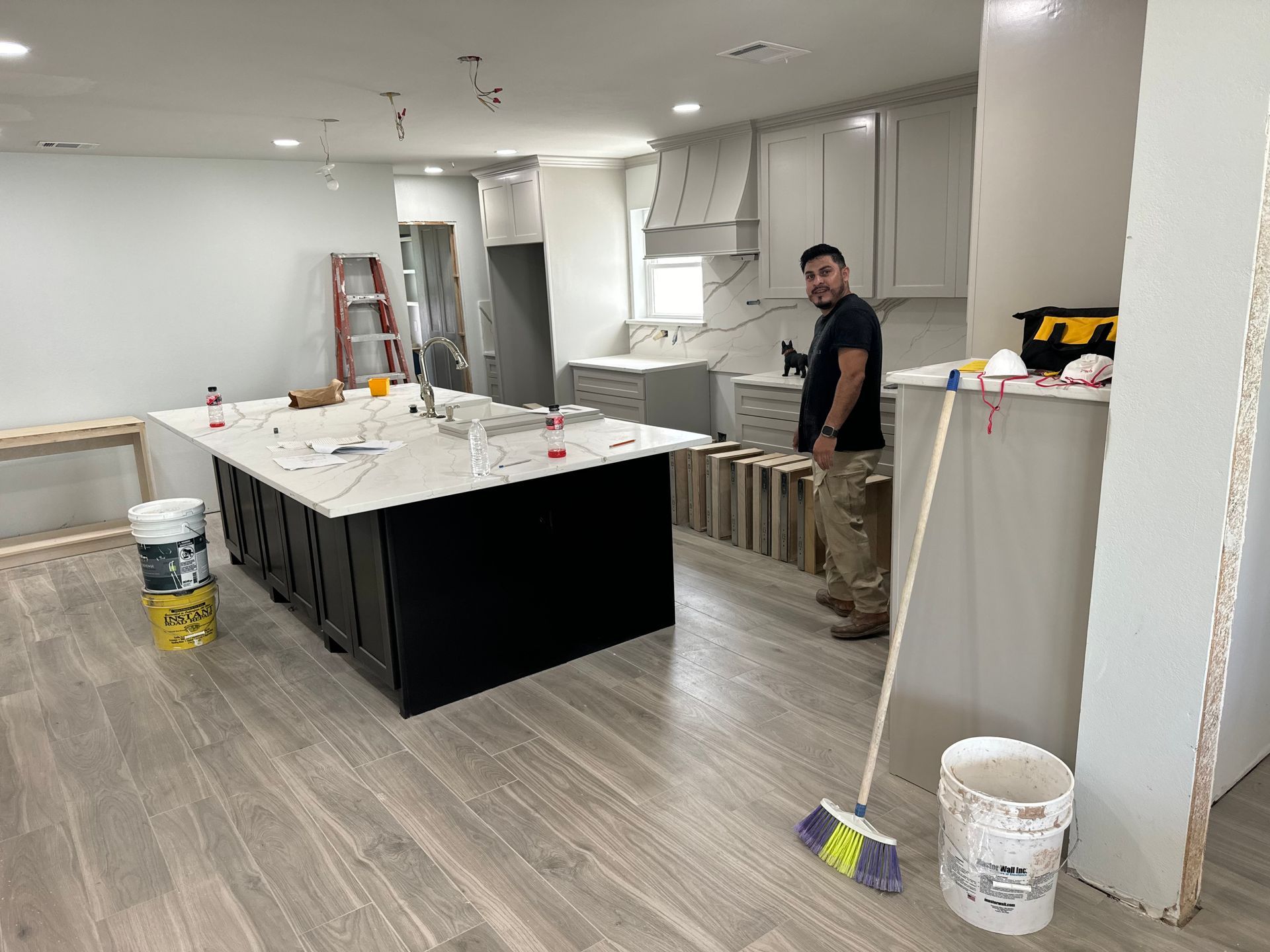 A man is standing in a kitchen with a broom.