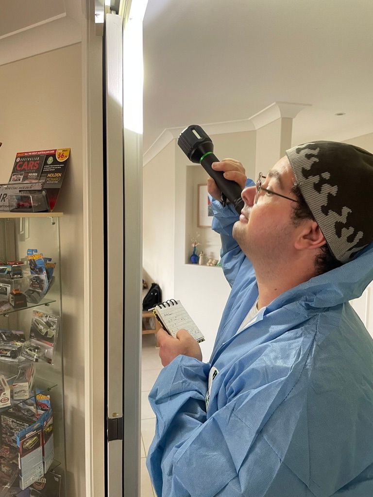 Person in blue coveralls examines a doorway with a flashlight. He's wearing a hat, looking up, holding a notepad. — NatureWise Pest Control In Port Macquarie, NSW