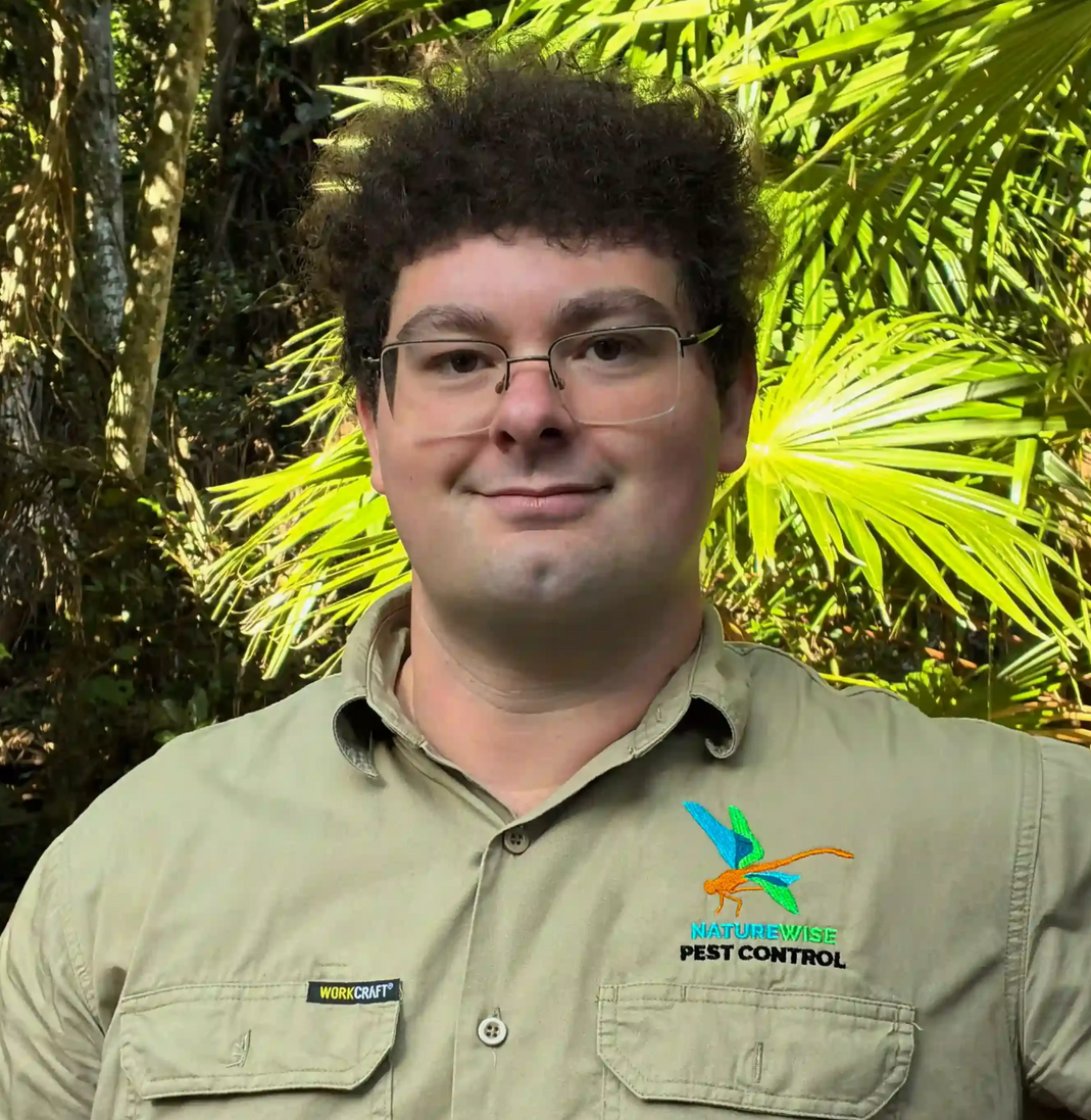 Man in tan work shirt smiles outdoors, with pest control logo.