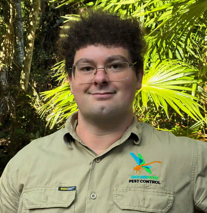 Man in tan work shirt smiles outdoors, with pest control logo.