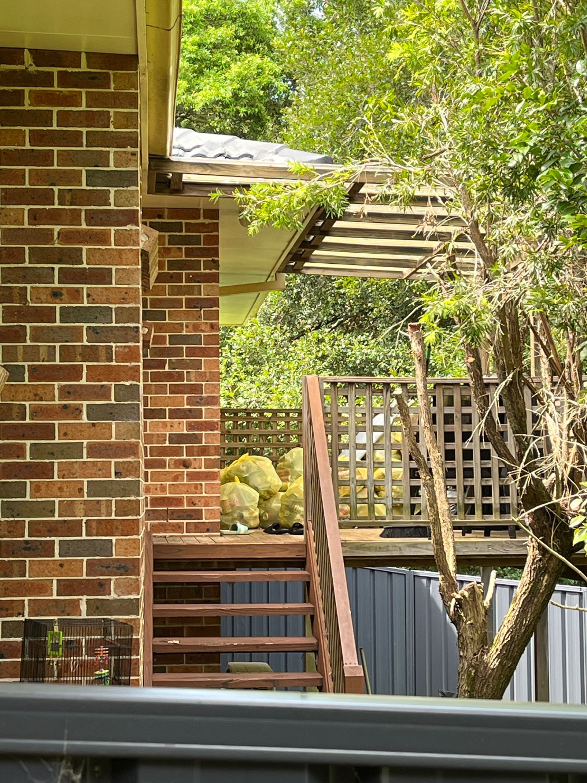 photo of neighboring house showing stairs, red brickwork and back deck. many bags of rubbish litter back entrance, attracting rodents leading to infestations. rodent rat pest control naturewise port macquarie nsw