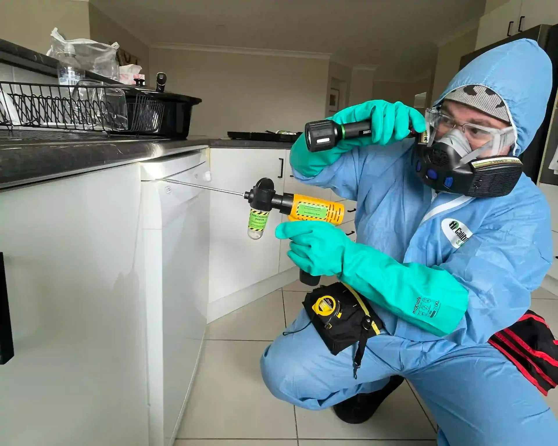 Person in protective suit using a drill, inspecting a kitchen cabinet — NatureWise Pest Control In Port Macquarie, NSW