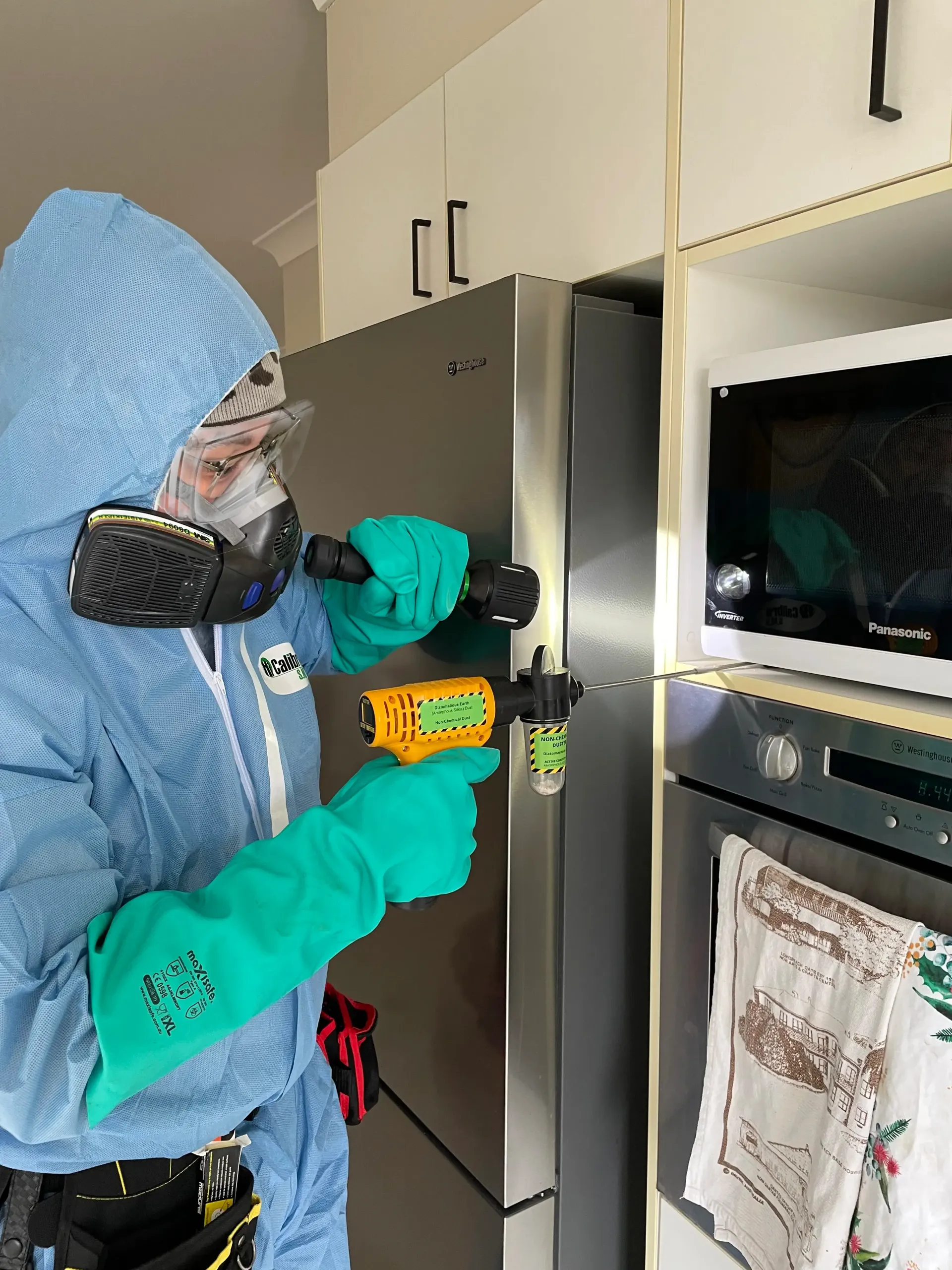 Person in Protective Suit Inspecting a Refrigerator — NatureWise Pest Control In Port Macquarie, NSW