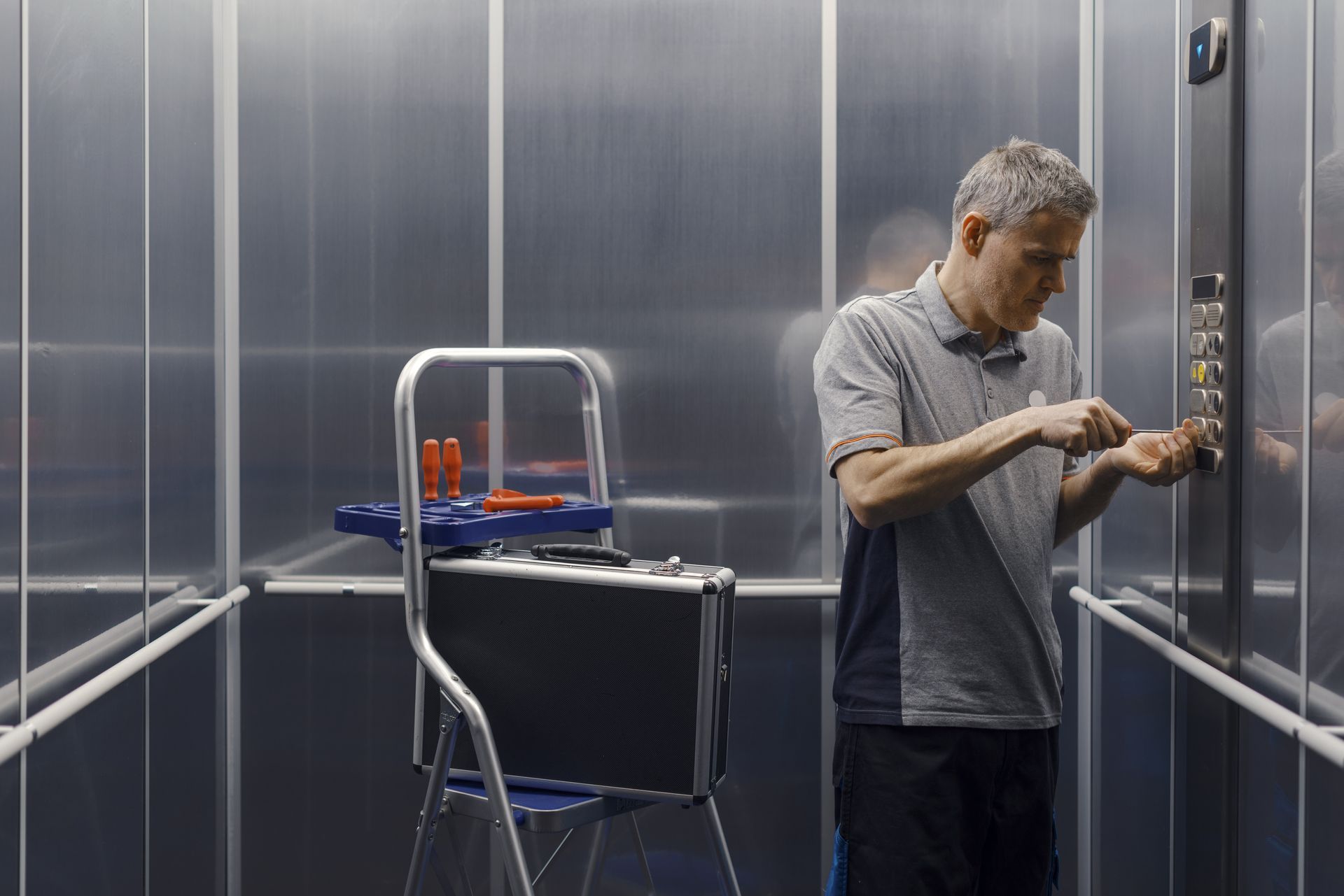 Man in elevator fixing control panel, tools on stepladder inside. Man in elevator fixing control panel, tools on stepladder inside.