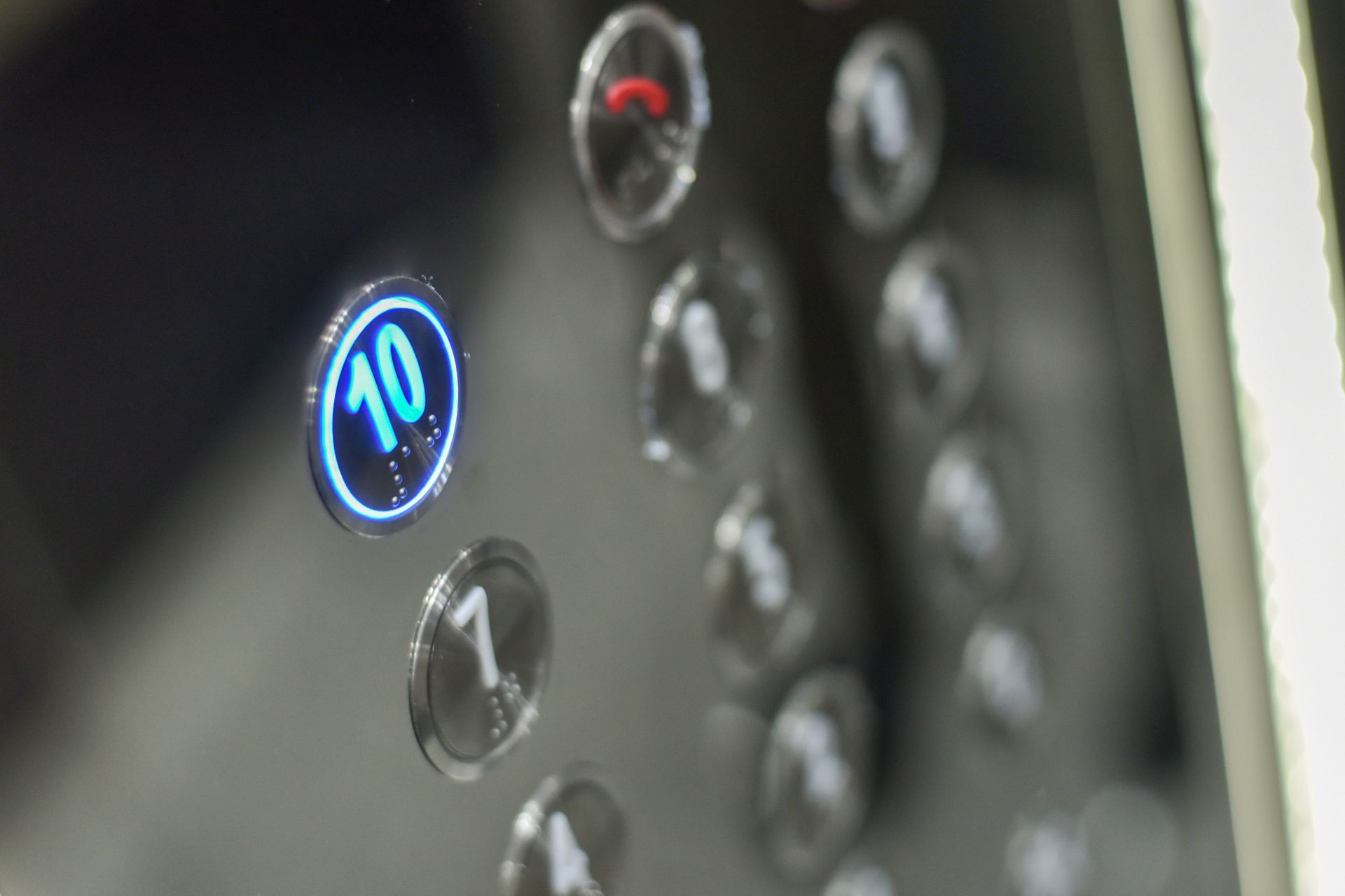 Close-up of elevator button panel, button 10 lit up with blue, other buttons blurred.