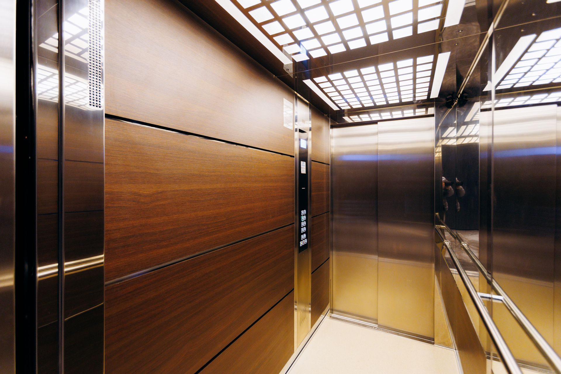 Inside of an elevator. Walls are wood paneling and stainless steel. Bright overhead lights. Inside of an elevator. Walls are wood paneling and stainless steel. Bright overhead lights.