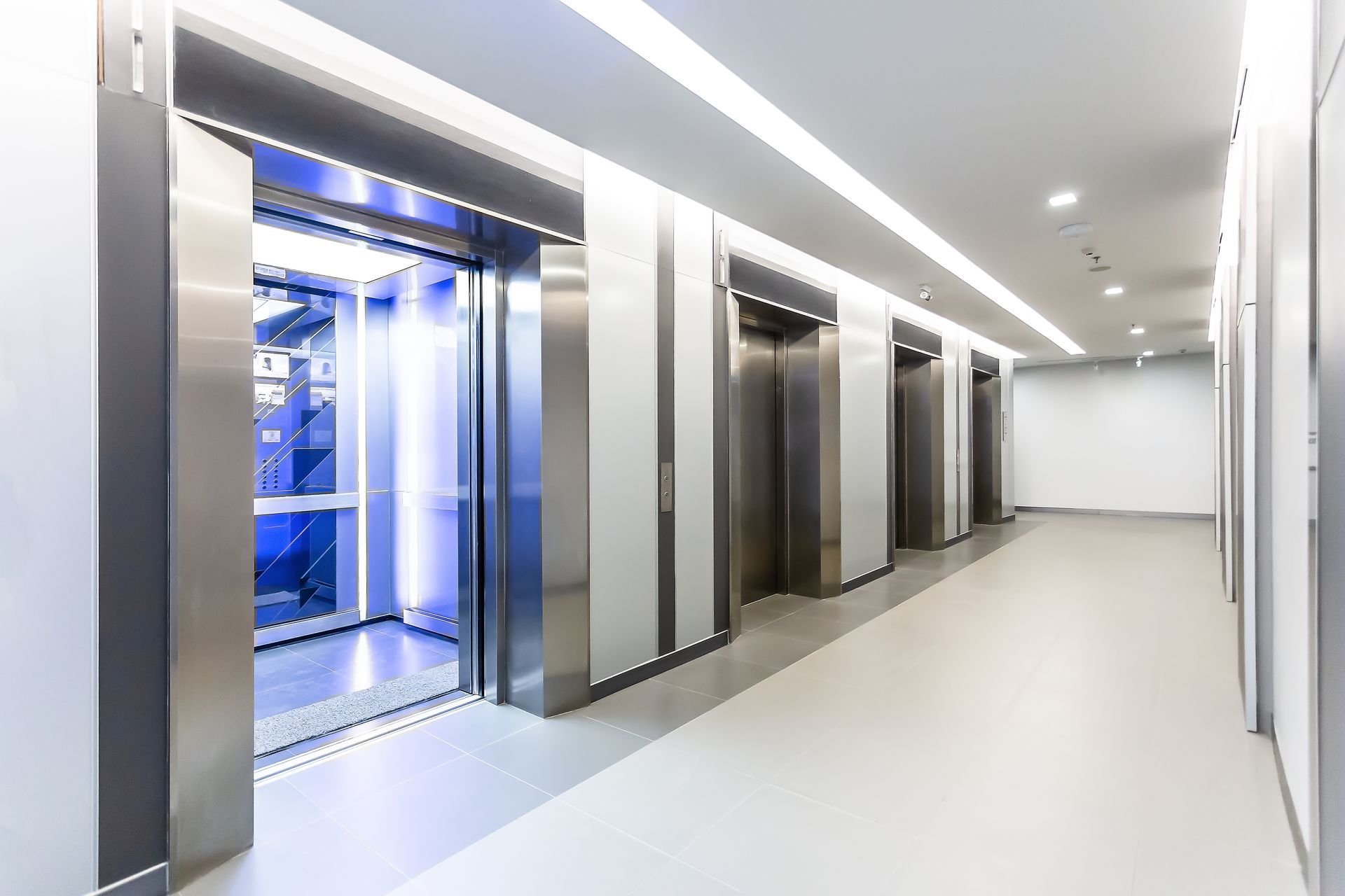 Hallway with several stainless steel elevators. One elevator door is open, with a blue-lit interior. Hallway with several stainless steel elevators. One elevator door is open, with a blue-lit interior.