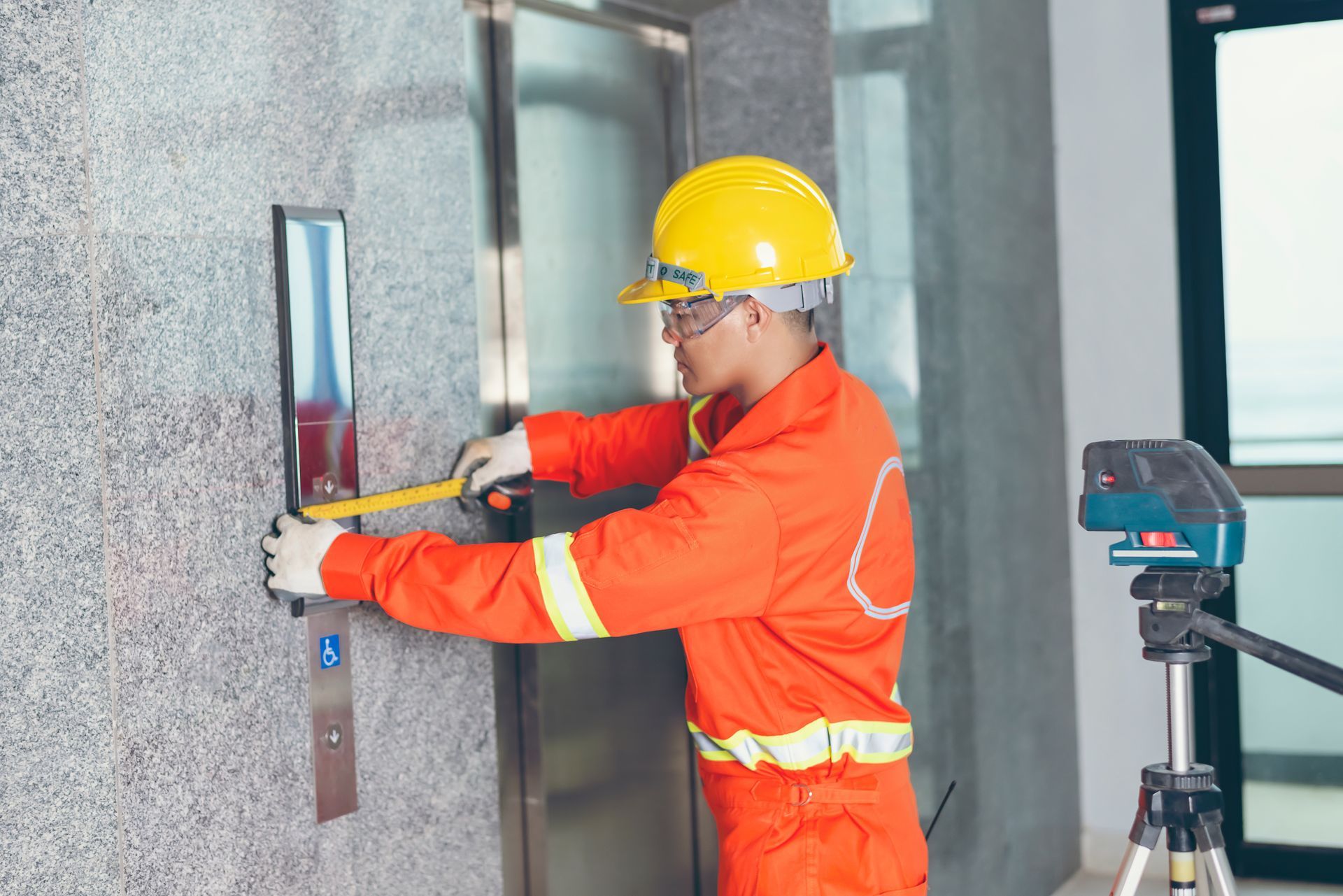Person in orange jumpsuit and hard hat measuring elevator buttons. Person in orange jumpsuit and hard hat measuring elevator buttons.