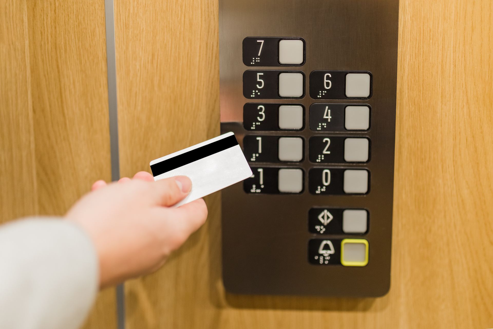 Person holding a card near an elevator control panel to activate floor selection. Person holding a card near an elevator control panel to activate floor selection.