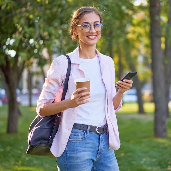 A woman is holding a cup of coffee and a cell phone.