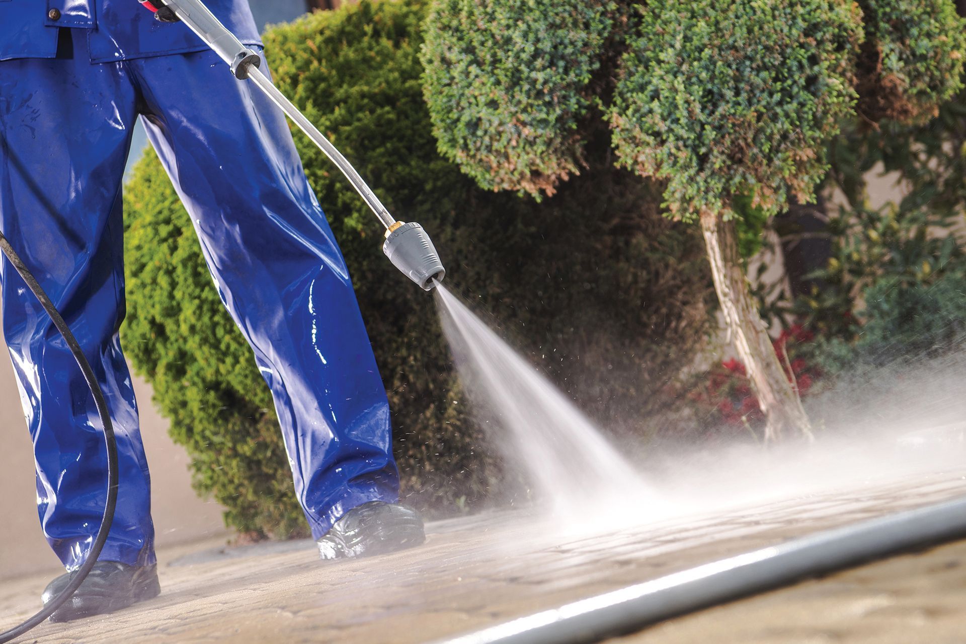 A man in blue pants is using a high pressure washer to clean a driveway.