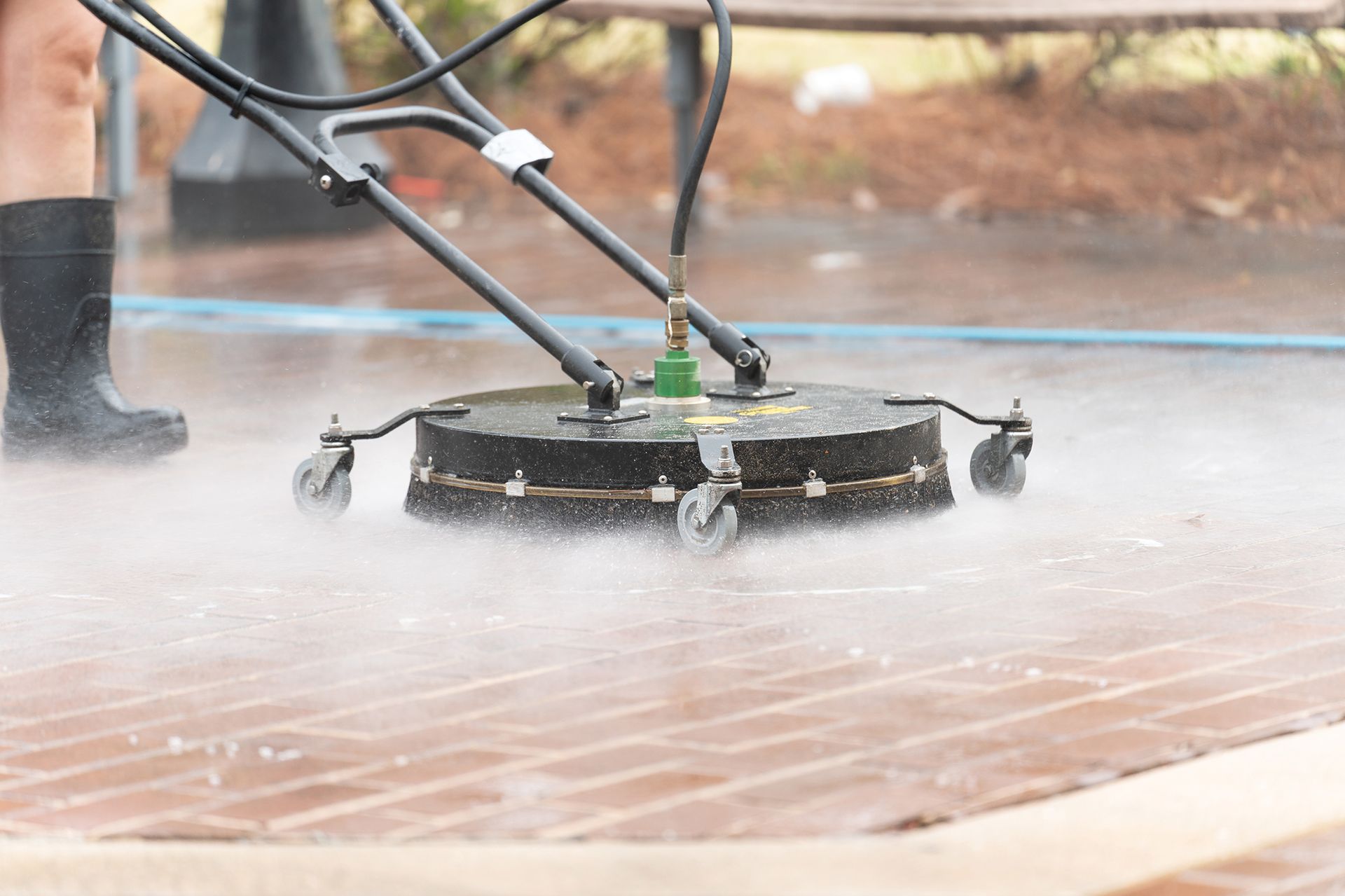 A person is using a high pressure washer to clean a brick walkway.