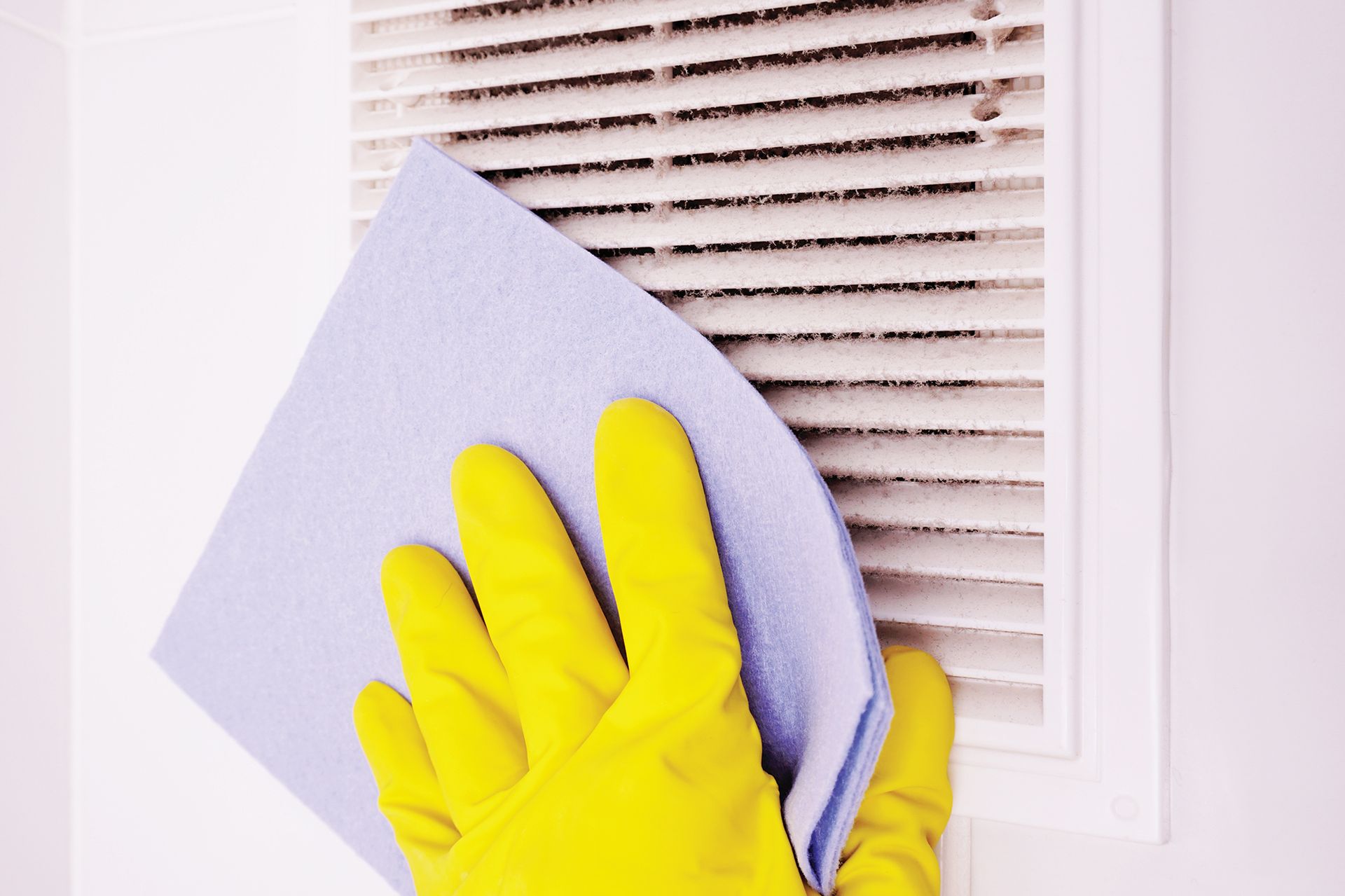 A person wearing yellow gloves is cleaning a vent with a cloth.
