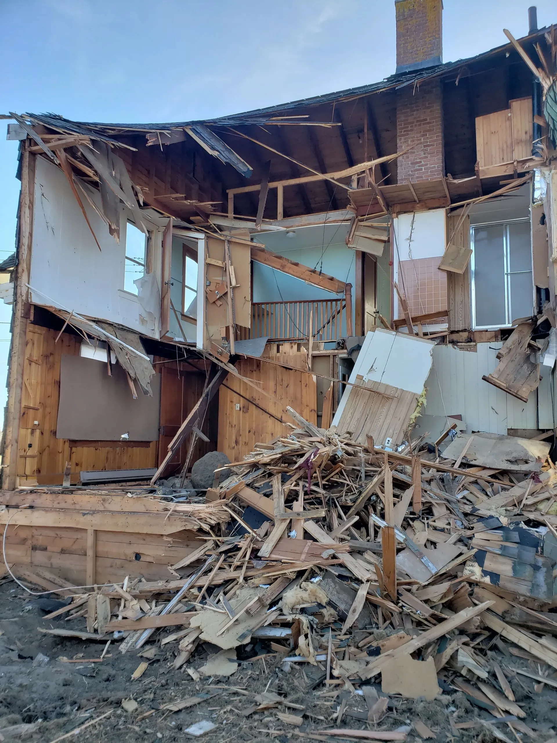 A house is being demolished and there is a pile of wood in front of it.