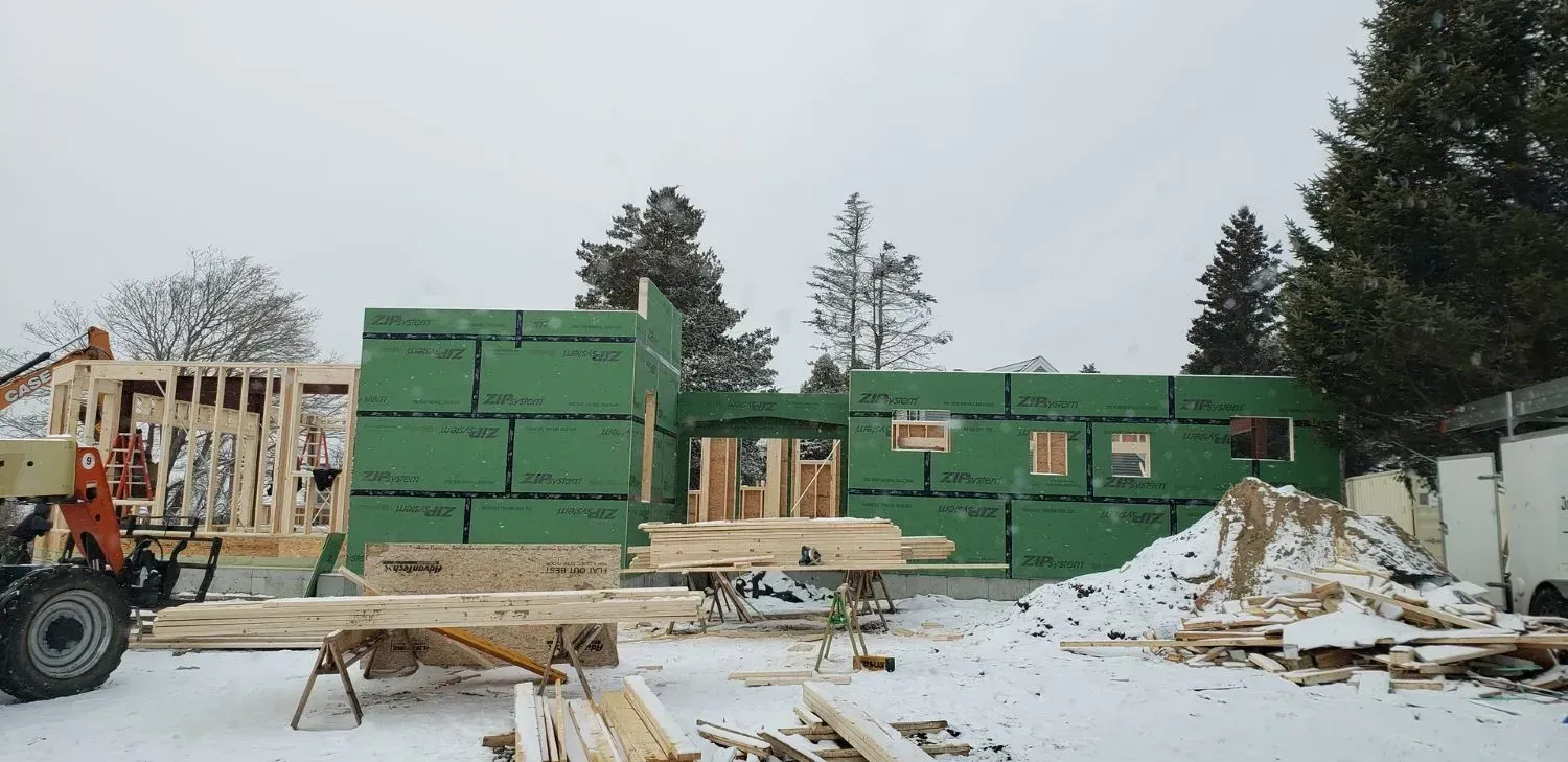 A house is being built in the snow with a tractor in the foreground.
