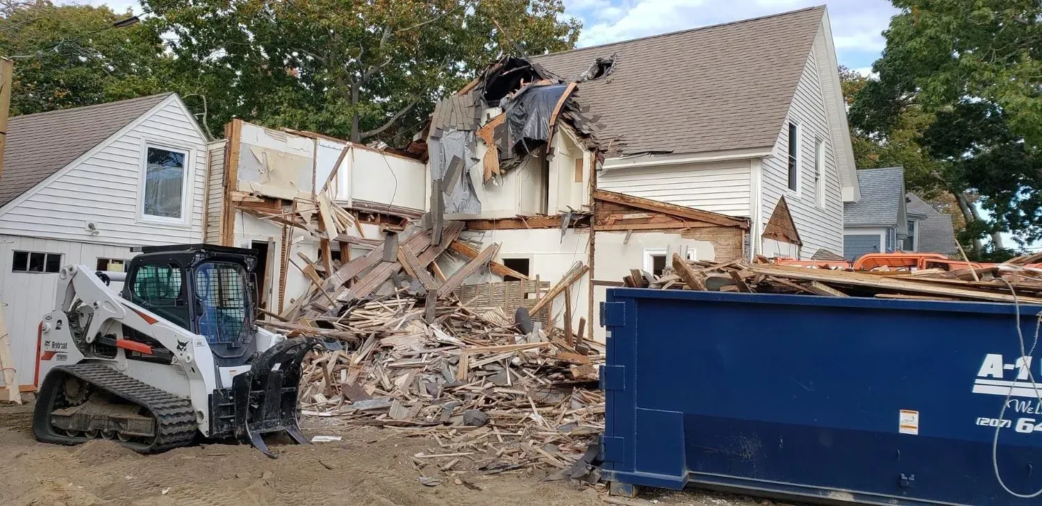 A house is being demolished with a bulldozer and a dumpster.