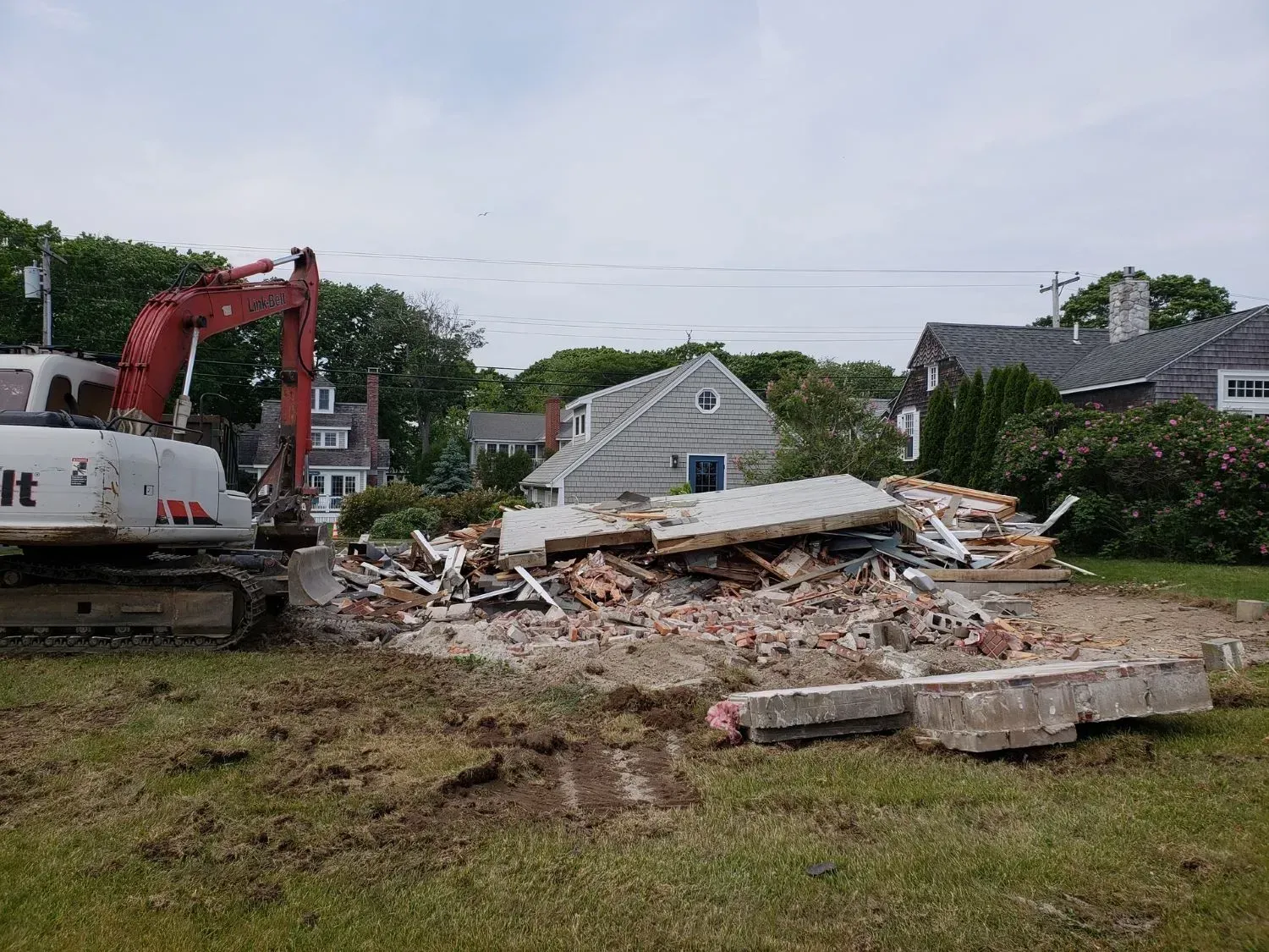 An excavator is demolishing a house in a grassy field.