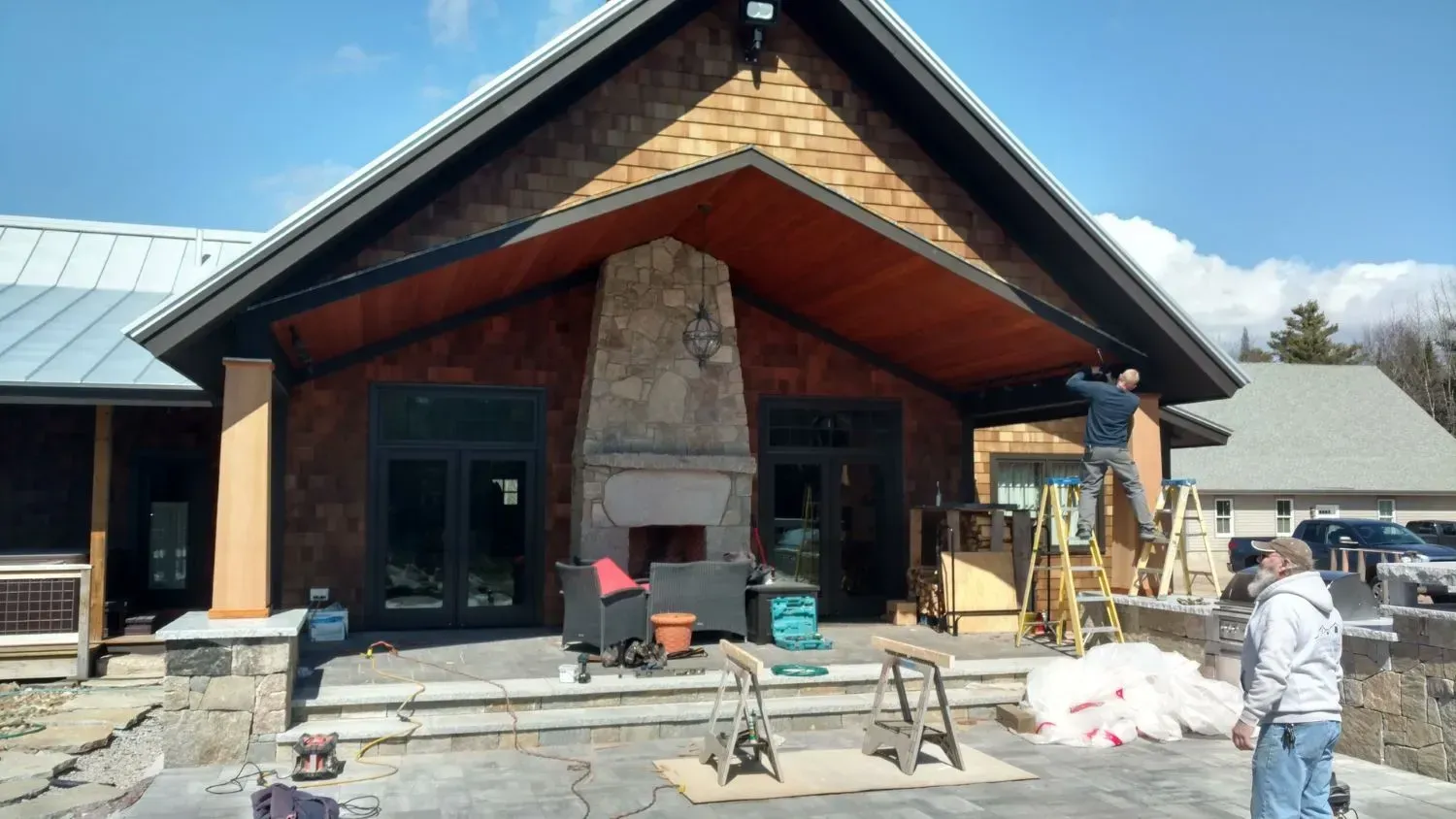 A man is standing on a ladder in front of a house with a fireplace.
