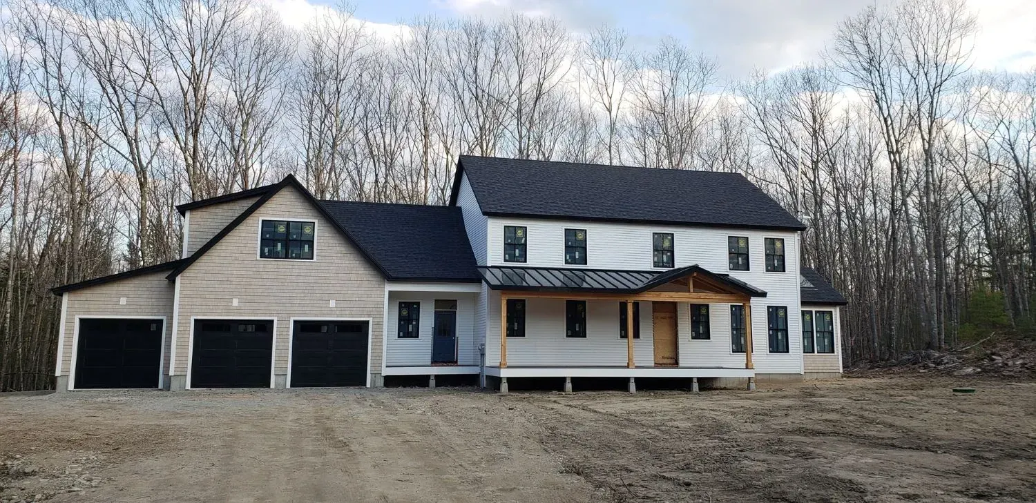 A large white house with a black roof is surrounded by trees.