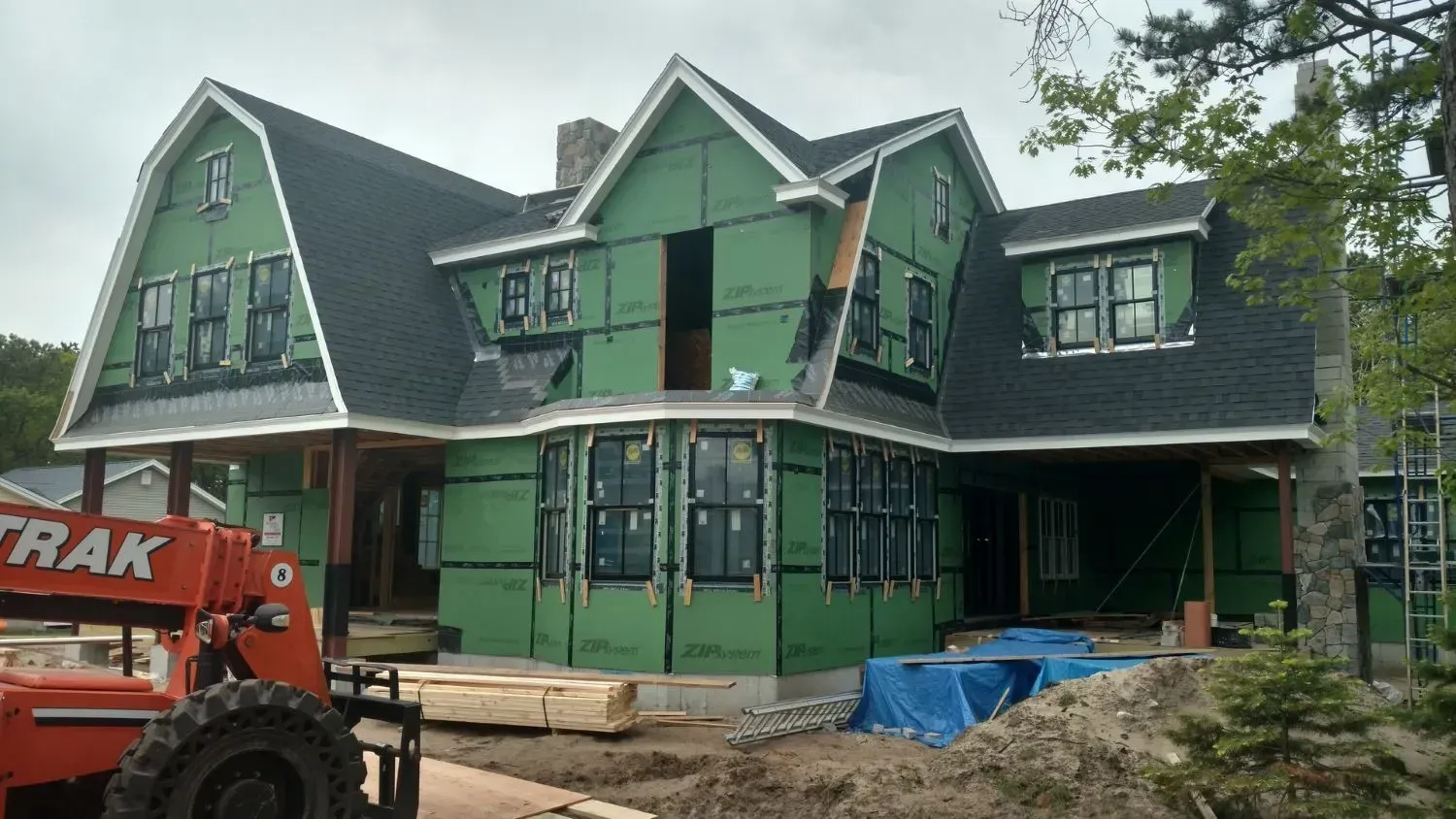 A large house is being built and a forklift is parked in front of it.