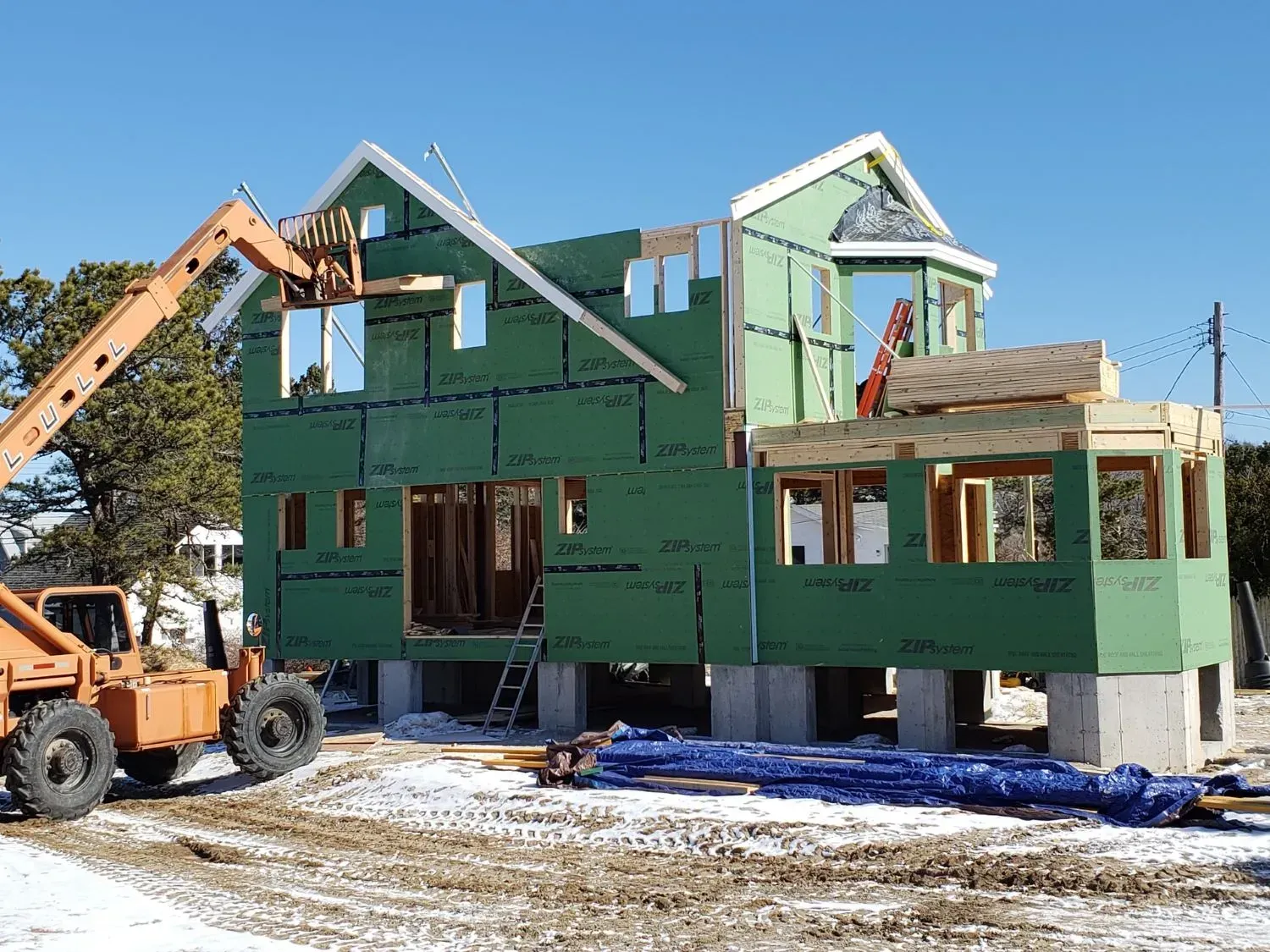 A house is being built in the snow with a crane in the background.