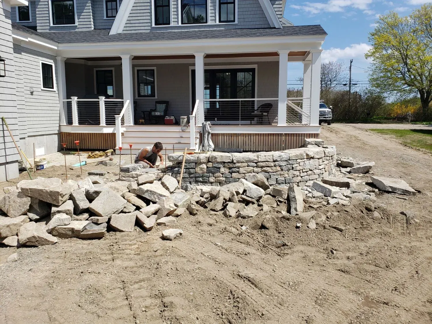 A man is working on a stone wall in front of a house.