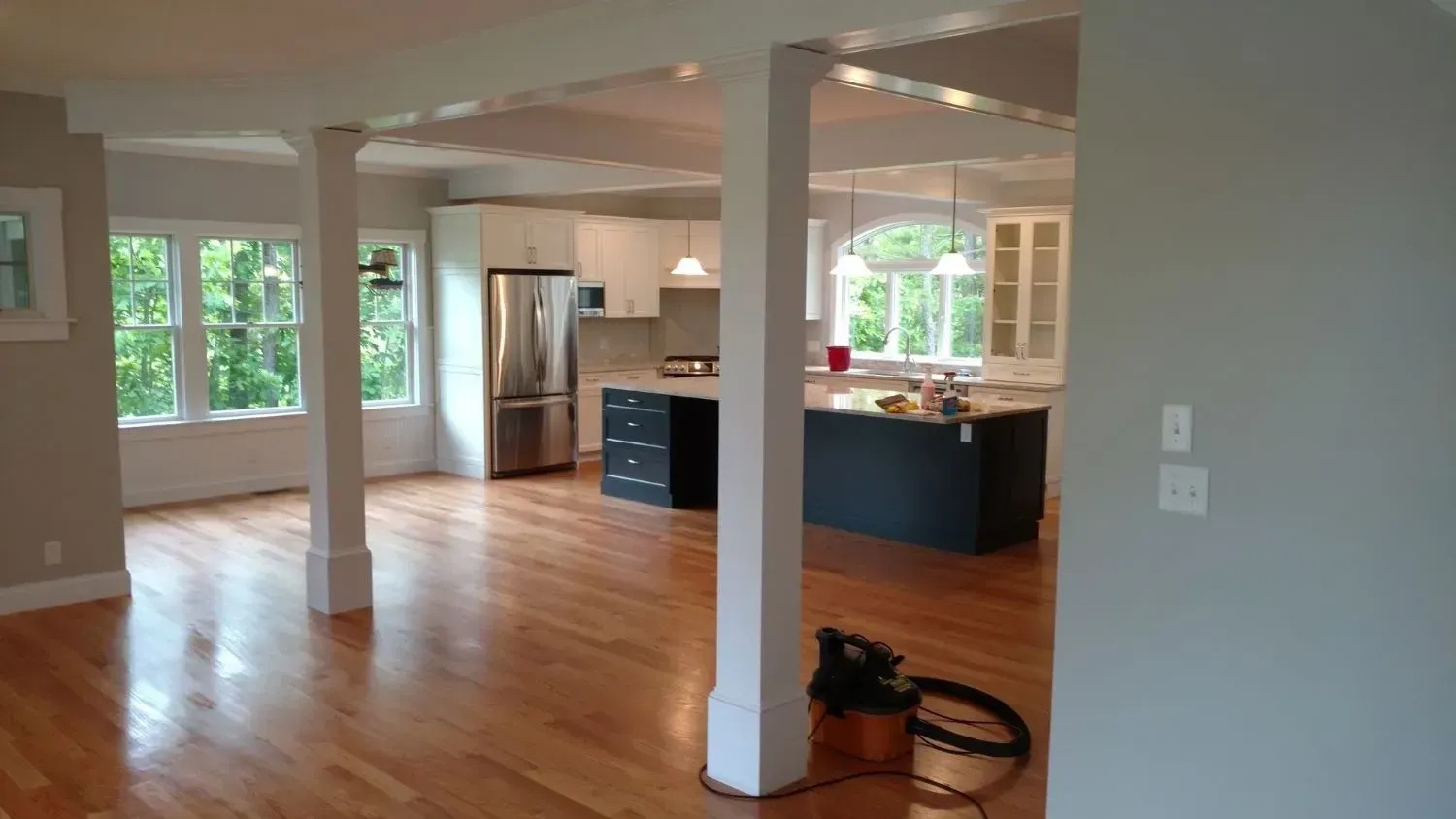 A large room with hardwood floors and a kitchen in the background.