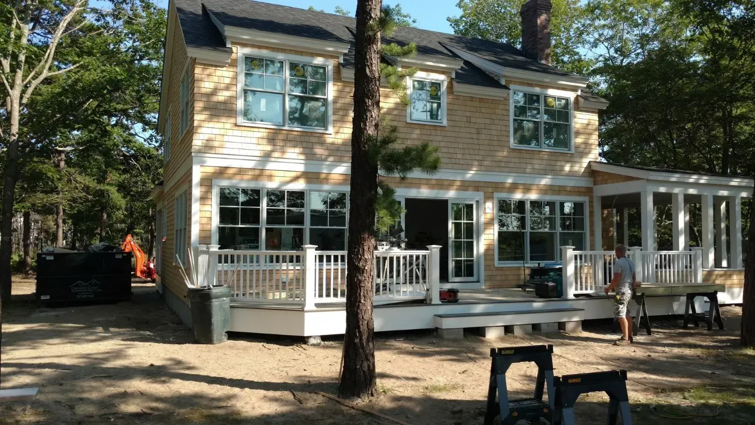 A man is standing in front of a large house with a large deck.