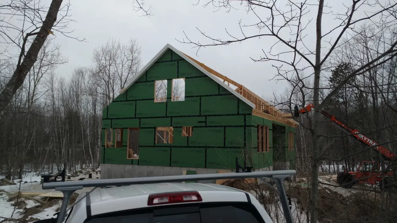 A car is parked in front of a house under construction.