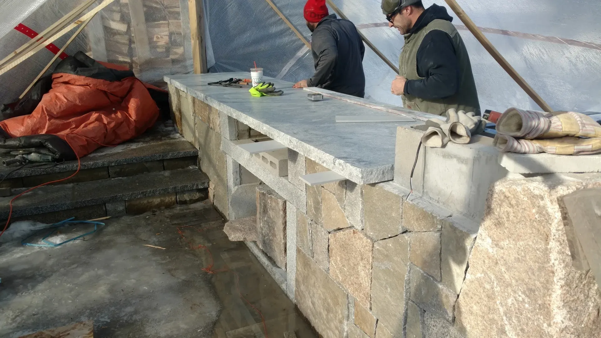 Two men are working on a stone wall.