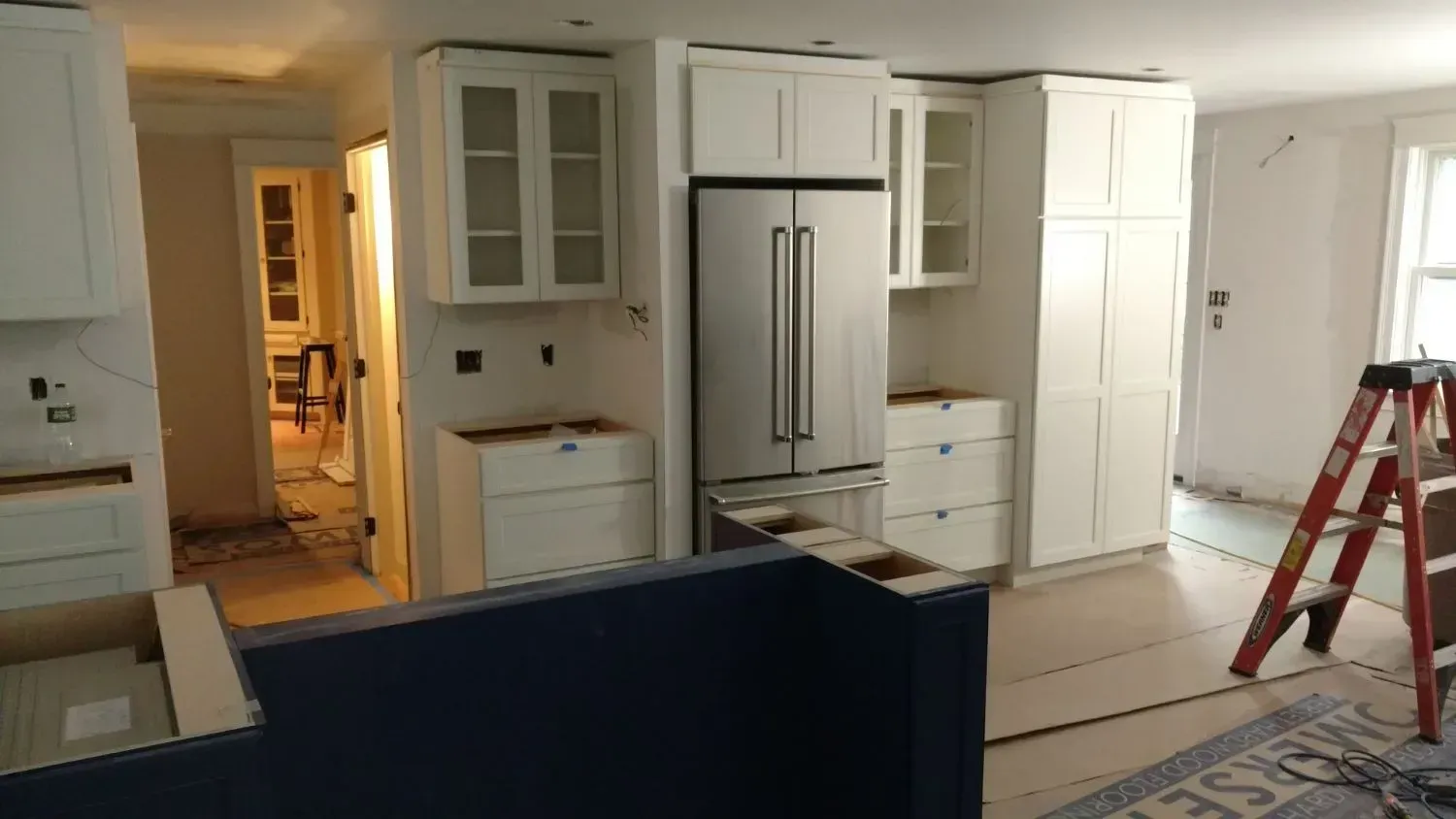 A kitchen under construction with white cabinets and a refrigerator.