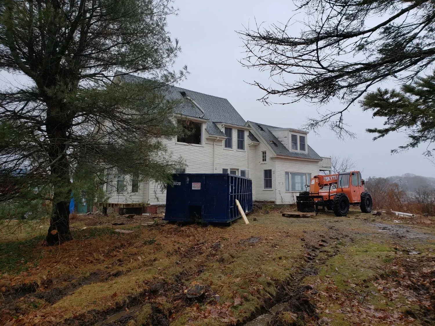 A large white house with a blue dumpster in front of it.