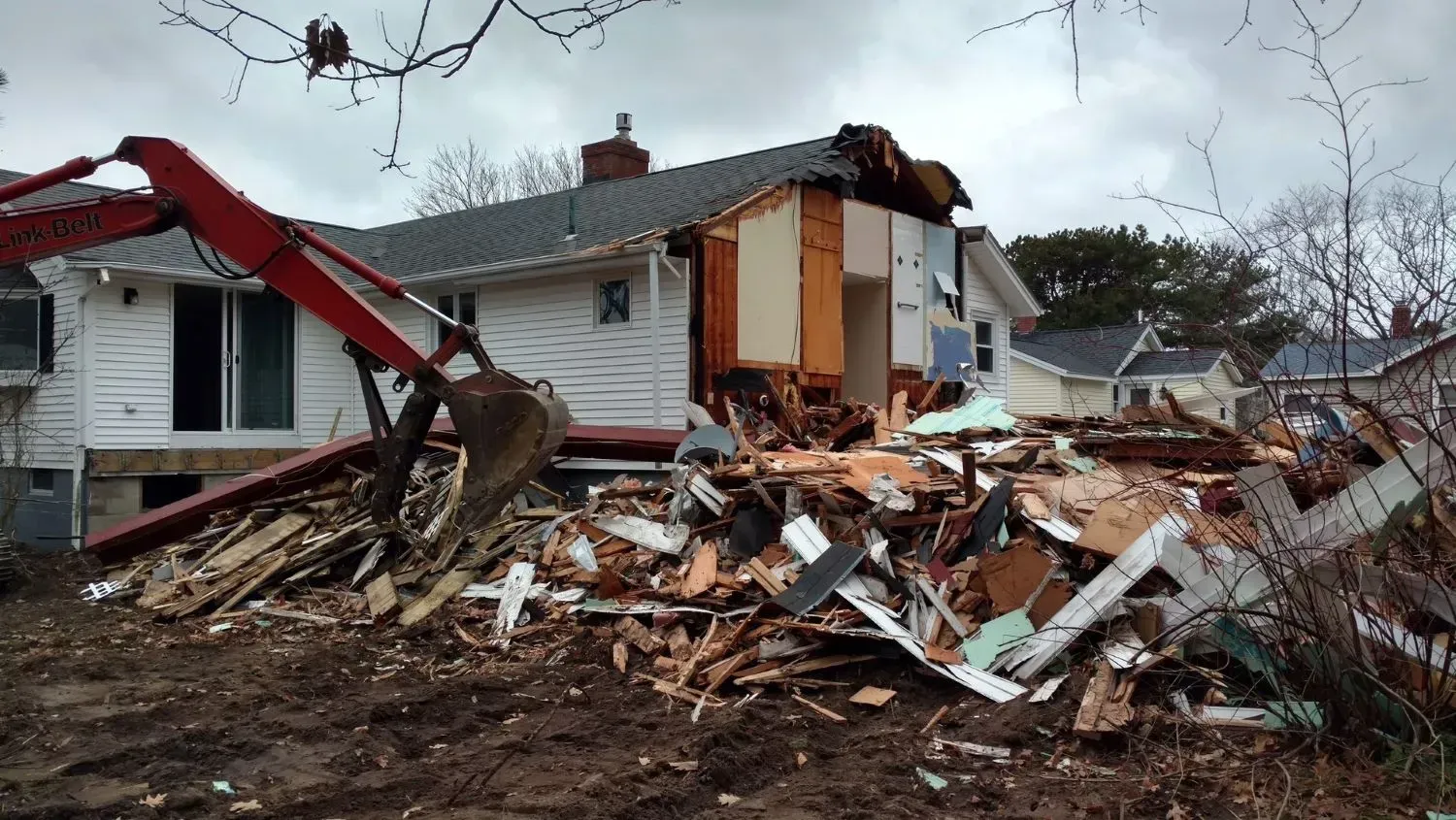 A house is being demolished by a red excavator.