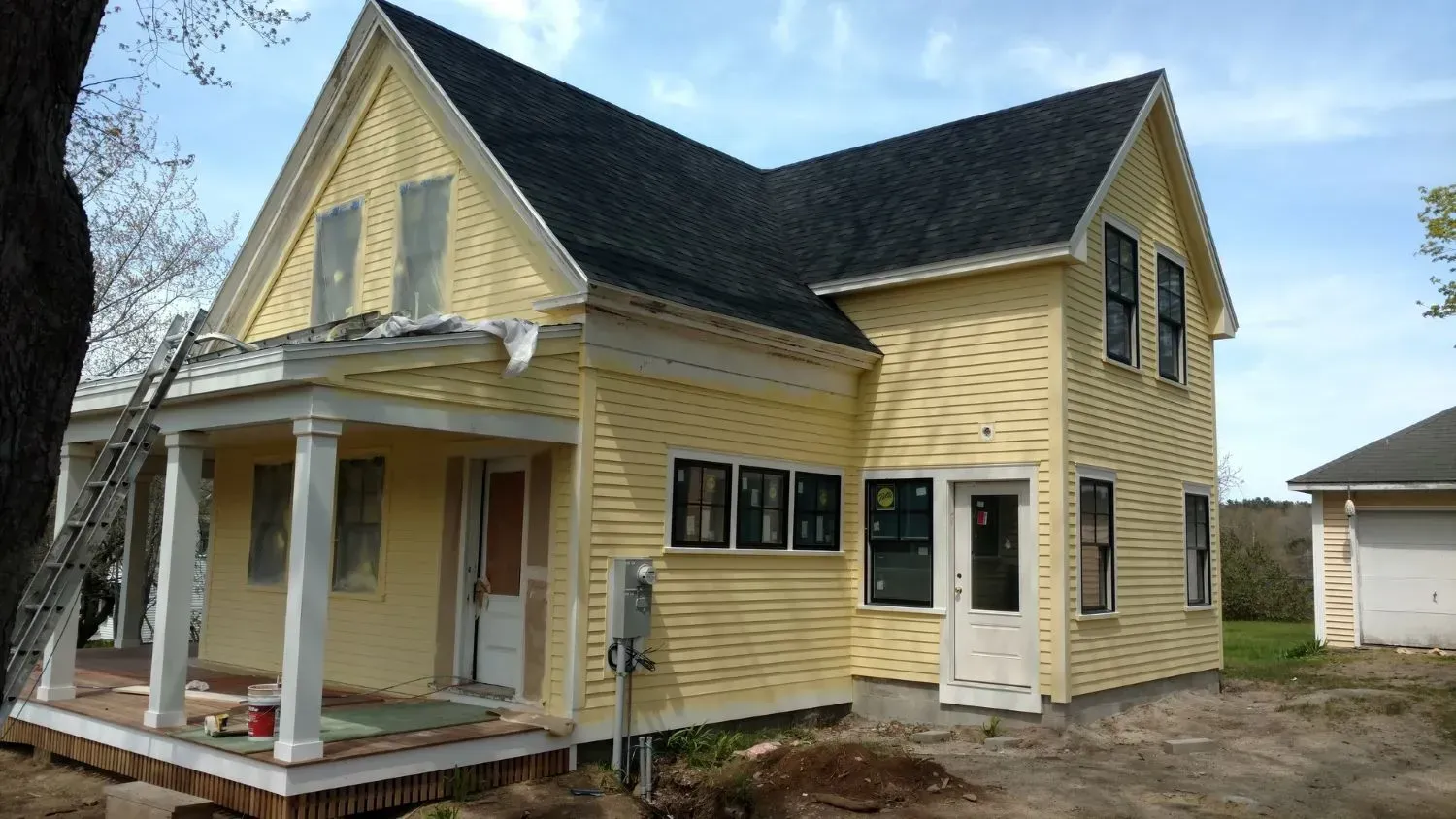 A yellow house with a black roof and a porch