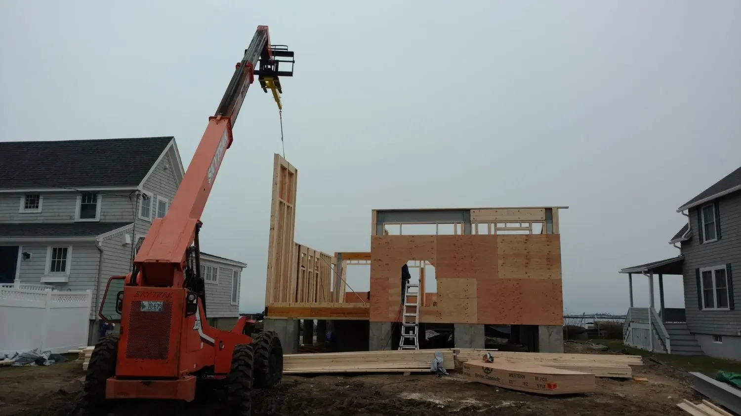 A forklift is lifting a piece of wood in front of a house under construction.