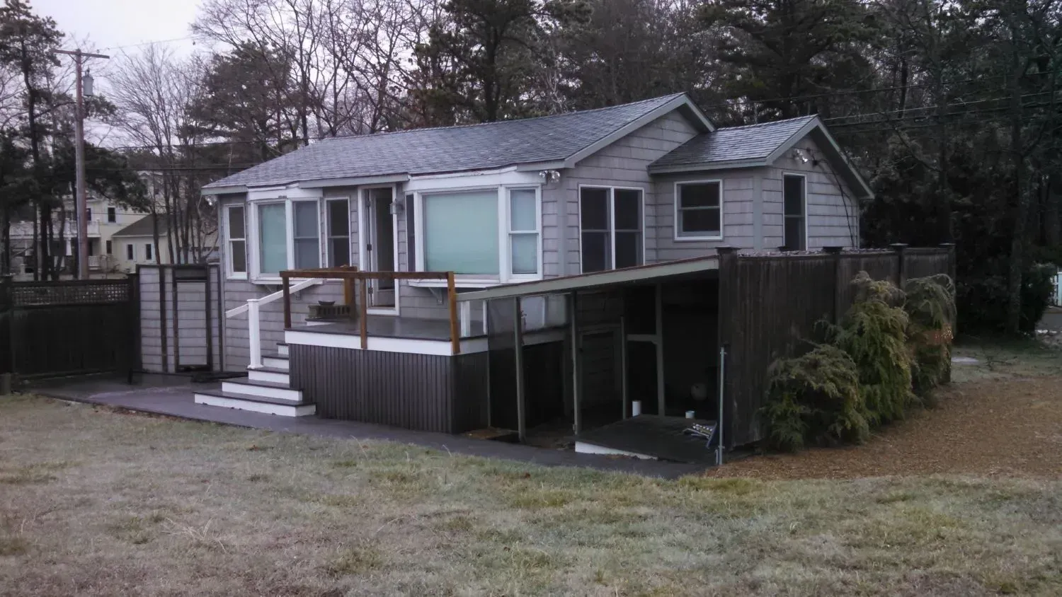 A small house with a porch and stairs is sitting in the middle of a grassy field.