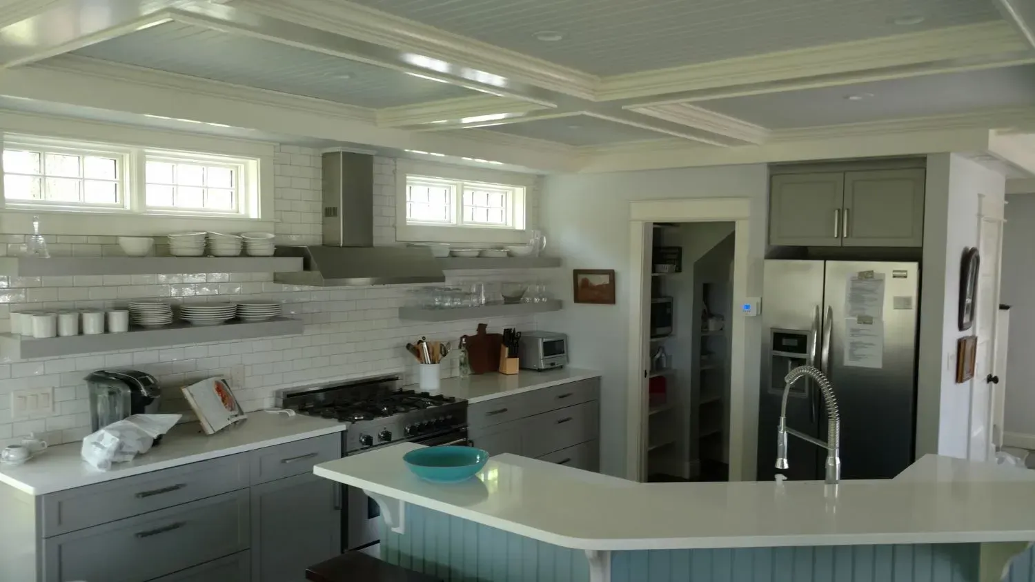 A kitchen with a stove , refrigerator , sink , and shelves.