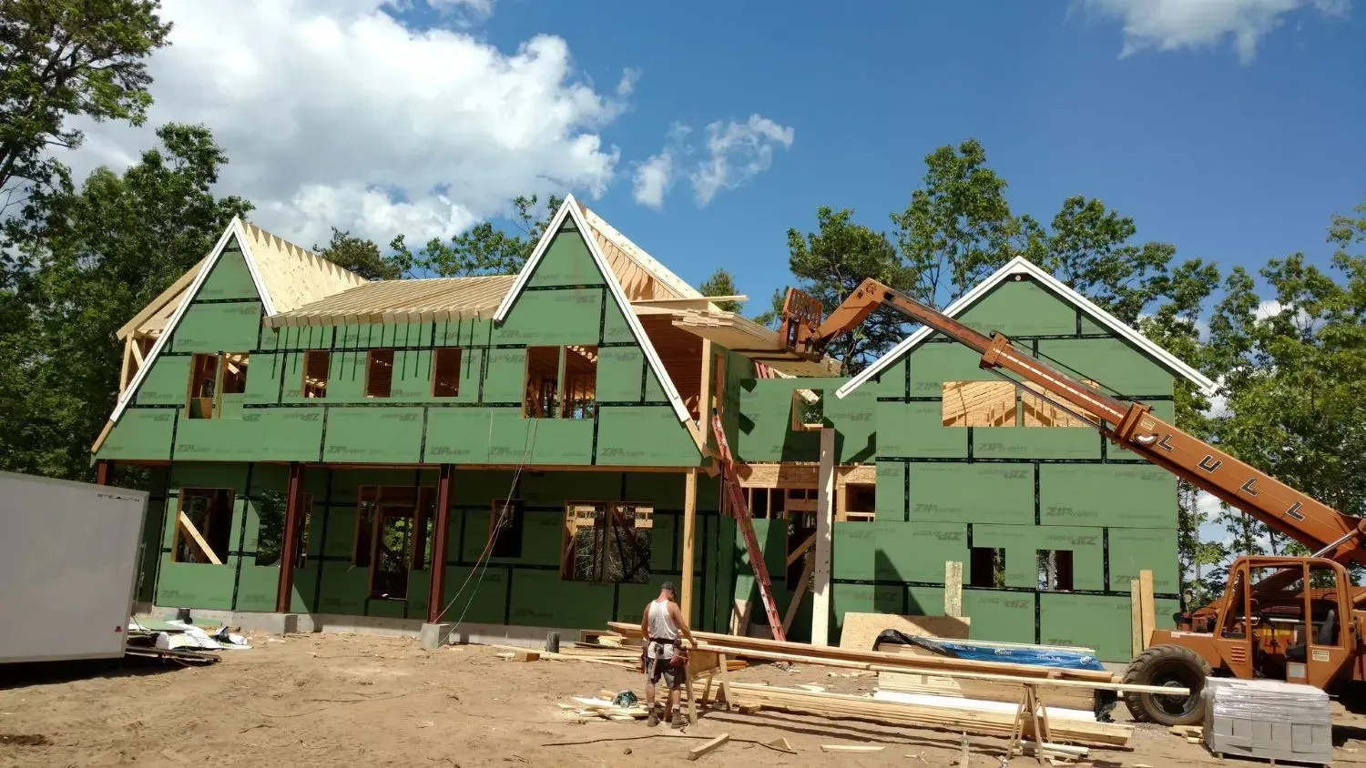 A large green house is being built with a forklift in front of it.